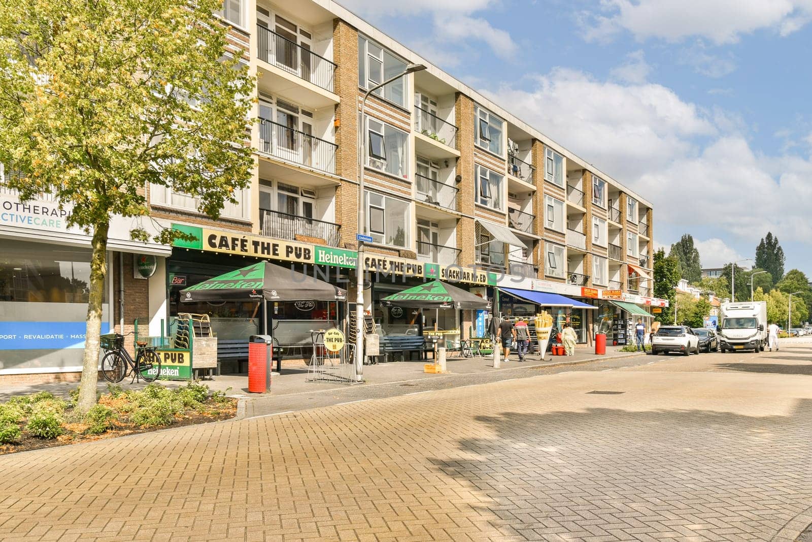A vibrant city street showcasing a contemporary cafe with outdoor seating, surrounded by modern residential buildings and greenery.