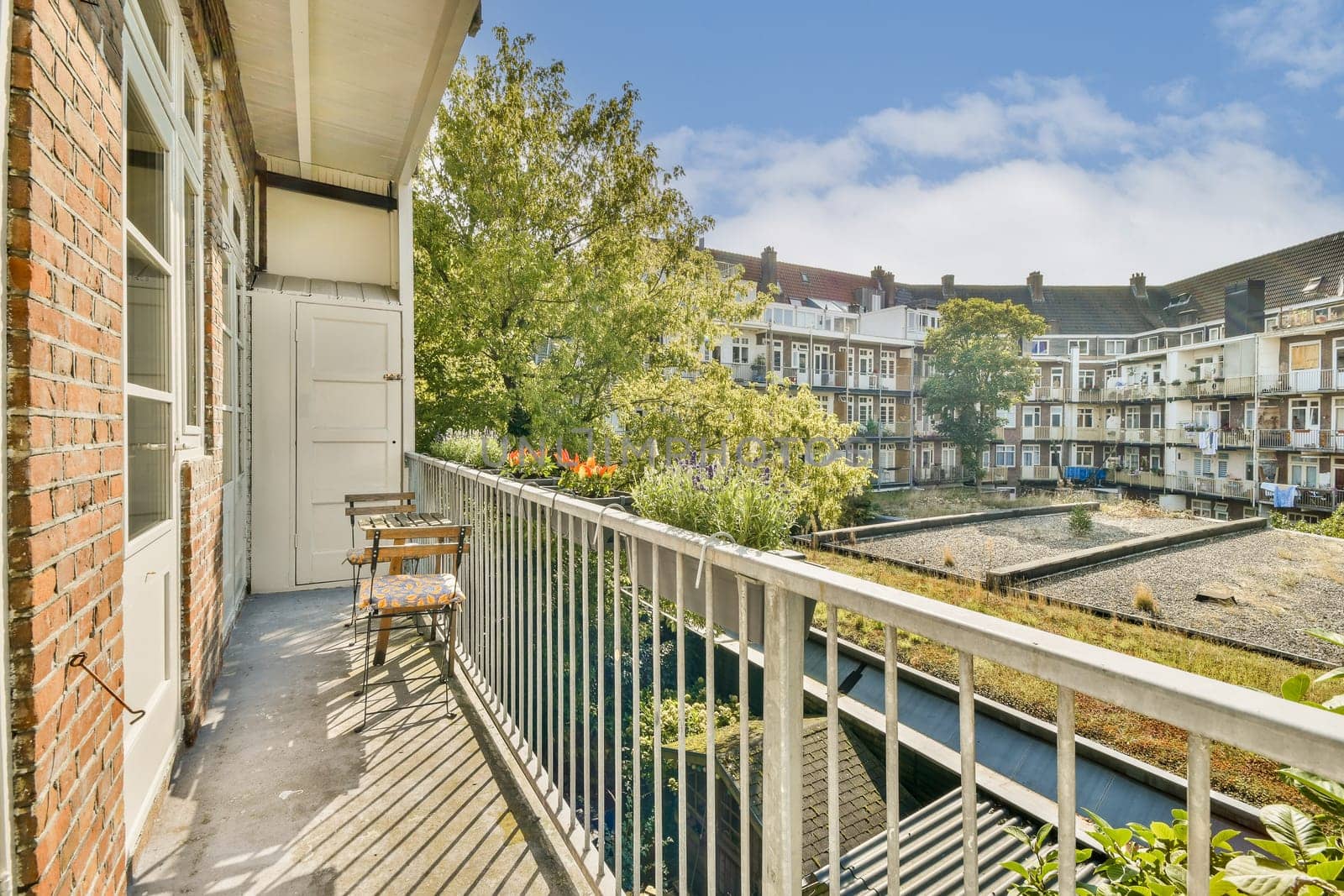 A serene balcony view showcasing lush greenery and cozy seating, framed by charming buildings in a peaceful urban courtyard on a sunny day.