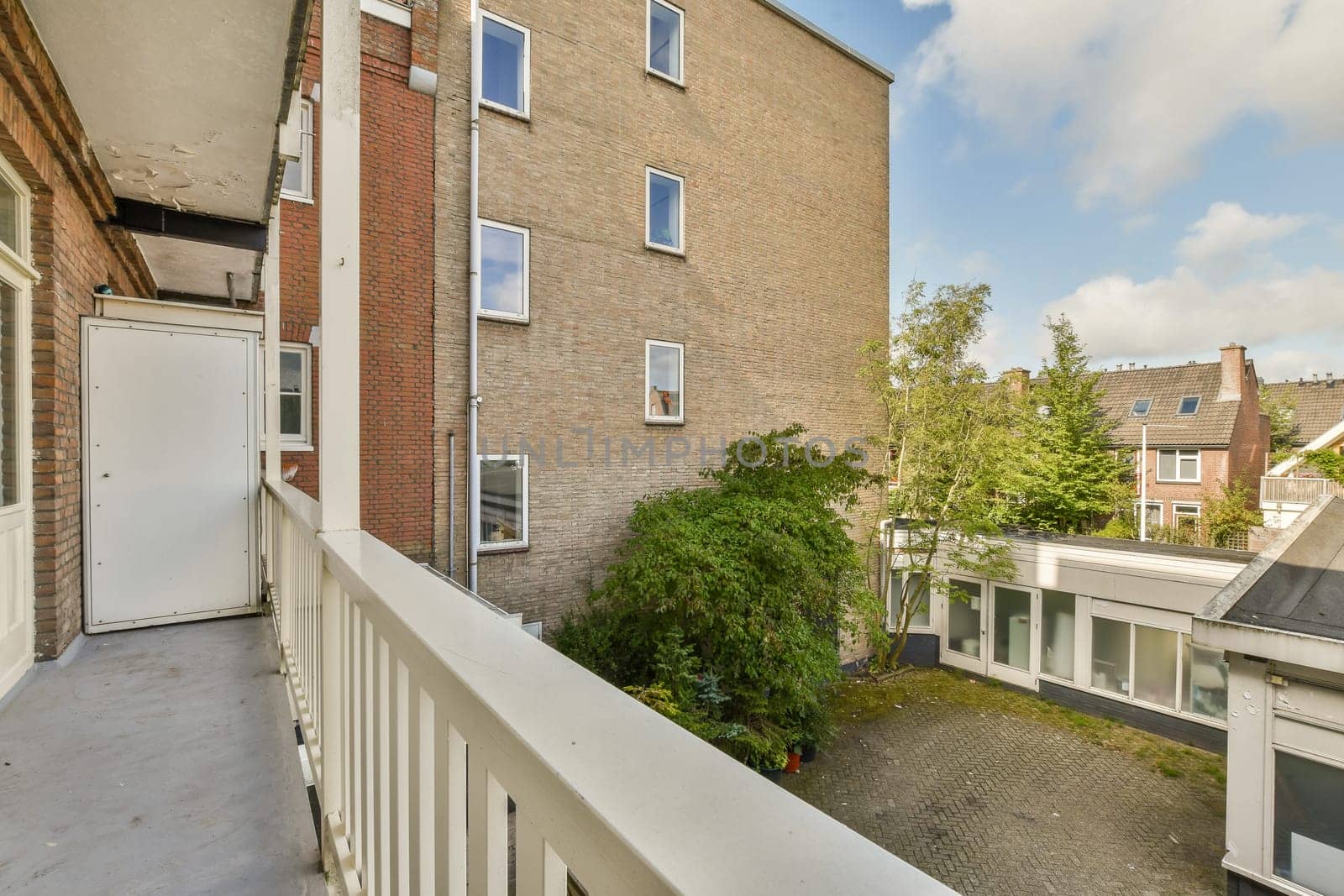 A modern urban apartment exterior showcasing a balcony view with greenery and nearby buildings, highlighting urban living and design.