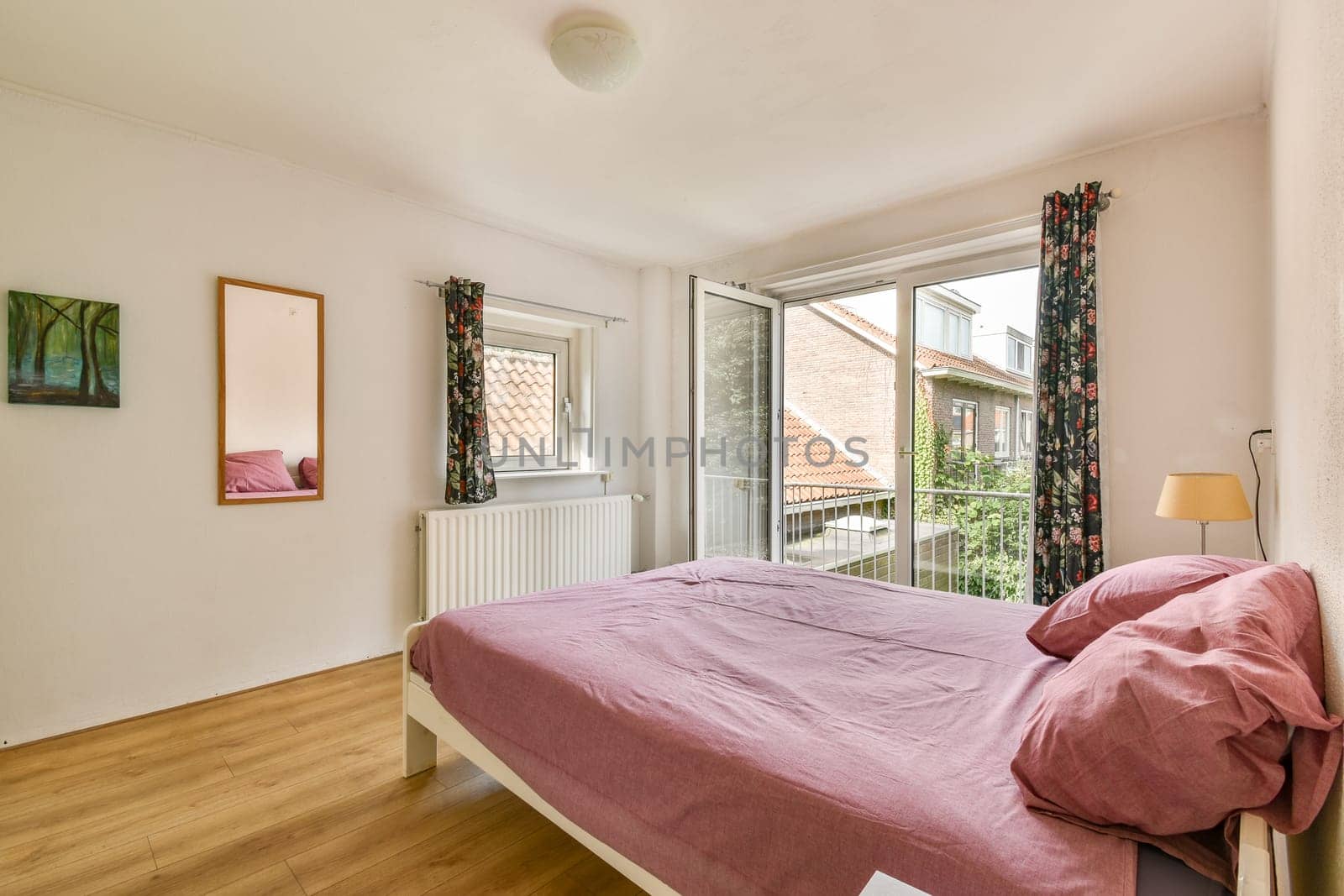 A bright and inviting bedroom featuring a comfortable bed, open window, and a mirror. Natural light enhances the warm atmosphere of the space.