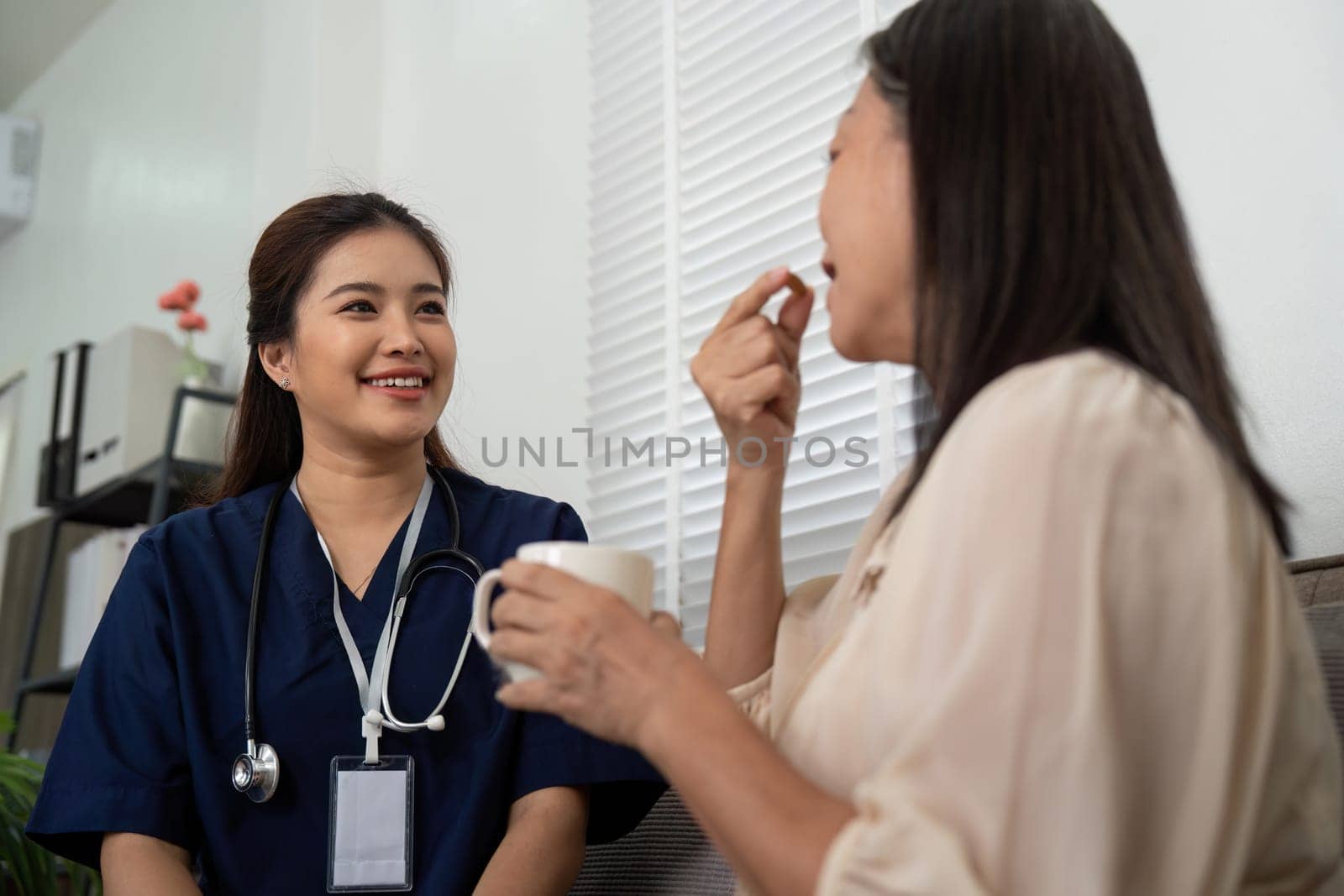During a home visit, a caregiver smiles at an elderly patient as she assists her with taking medication, enhancing both health and trust.