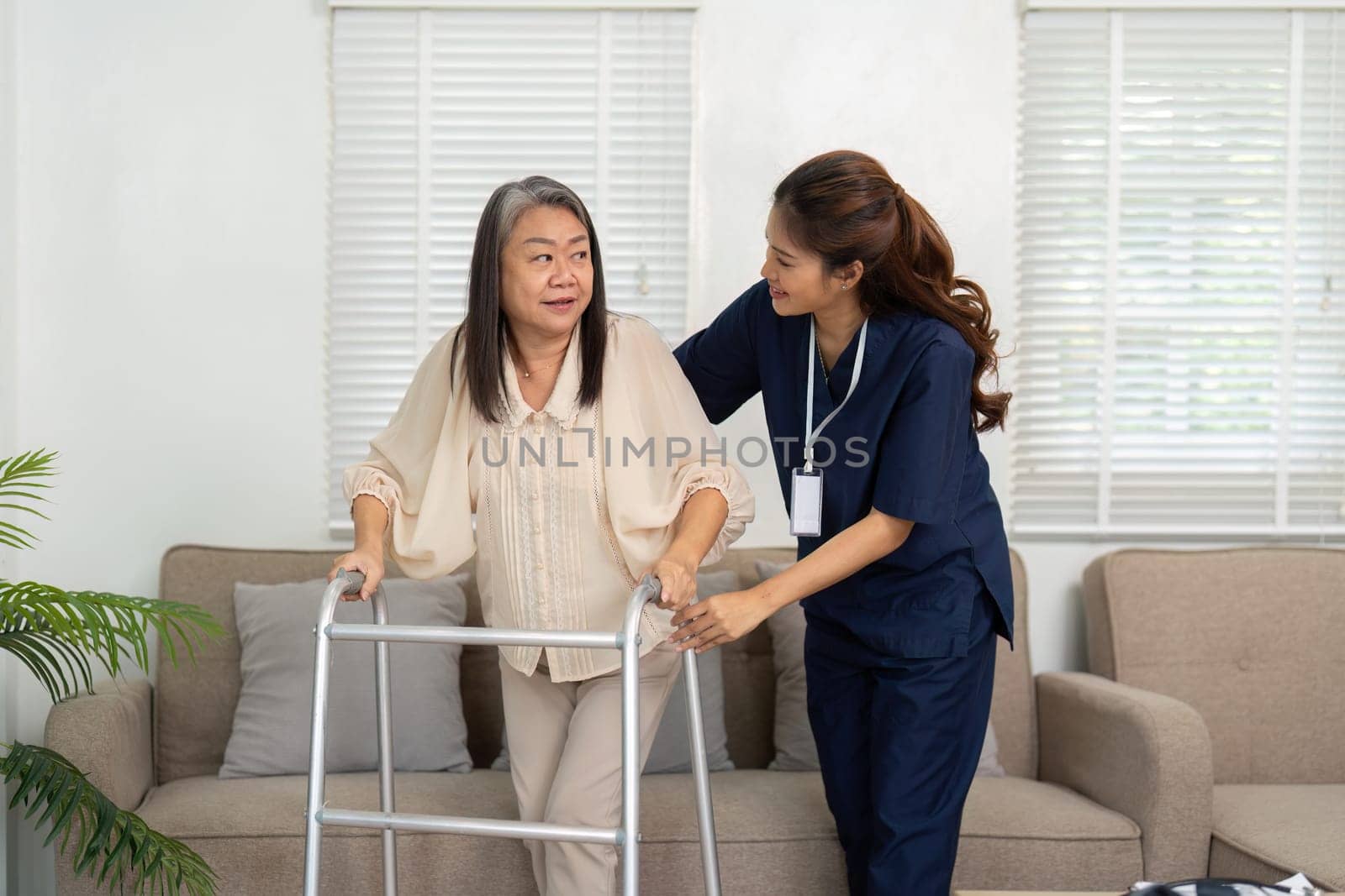 With a caring approach, the caregiver assists an elderly woman using a walker, promoting independence and mobility while ensuring her comfort.