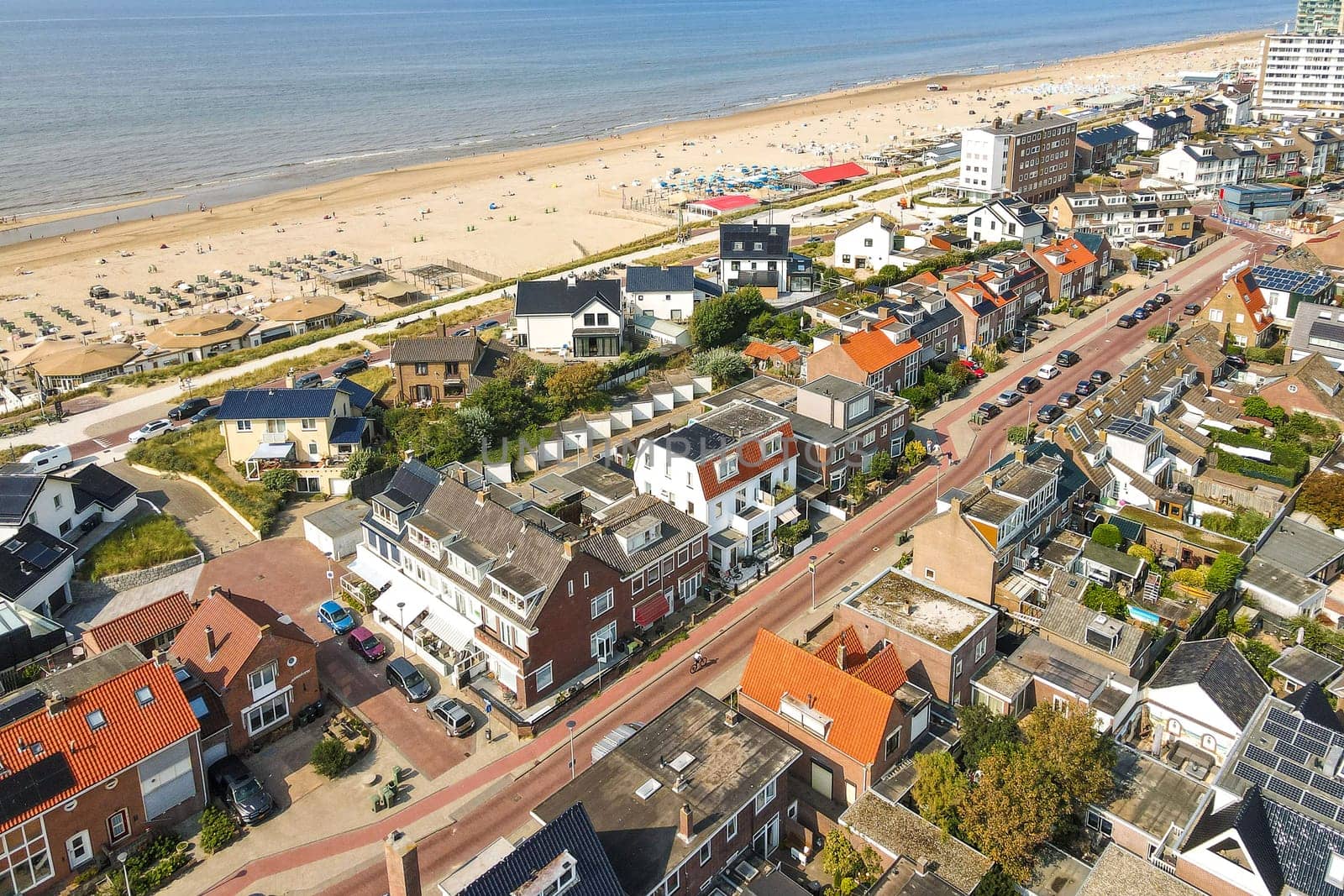 Featuring a charming coastal town, this aerial perspective showcases sandy beaches, residential areas, and vibrant beach activities, perfect for summer visits.