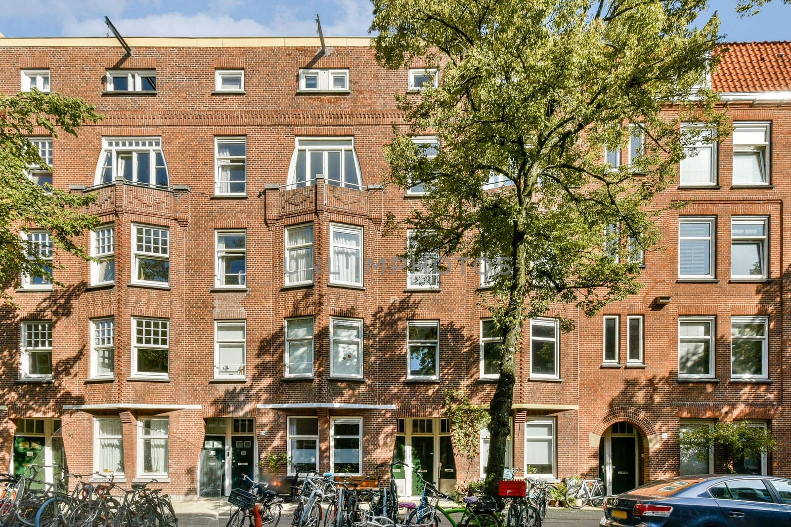 A charming red brick building featuring intricate architecture, adorned with windows and surrounded by greenery and bicycles. Captures the essence of urban life.