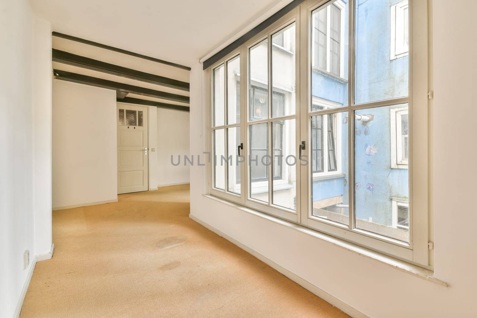 Bright interior space featuring expansive windows that allow natural light, complemented by soft texture flooring and a minimalist design.