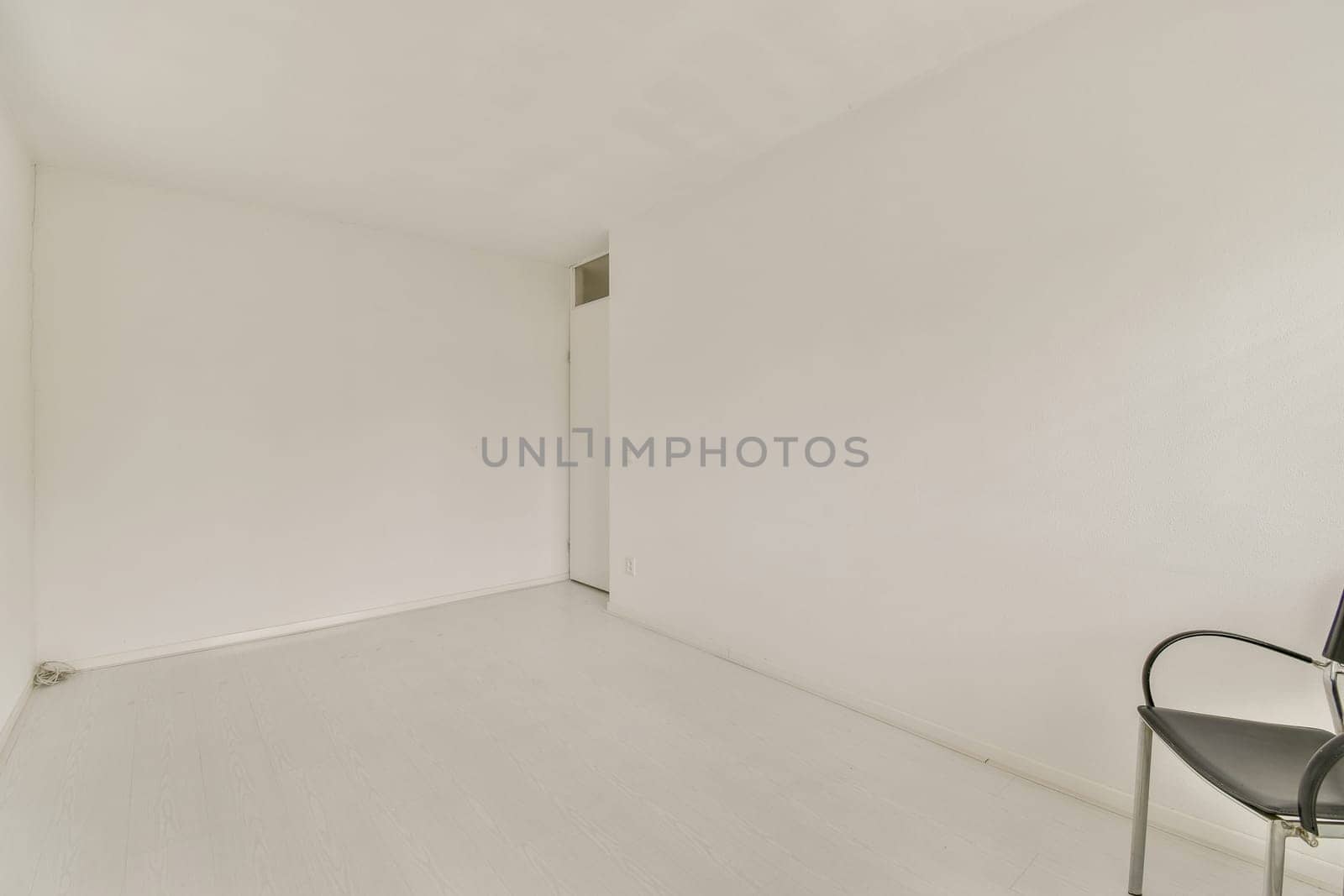A bright and spacious minimalist room featuring white walls and a simple design. The floor is light-colored, and the furnishings are minimal, enhancing the open feel.