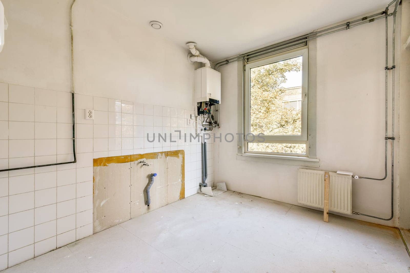 A vacant room showcasing white walls and utilities such as a window, radiator, and plumbing fixtures, awaiting completion.