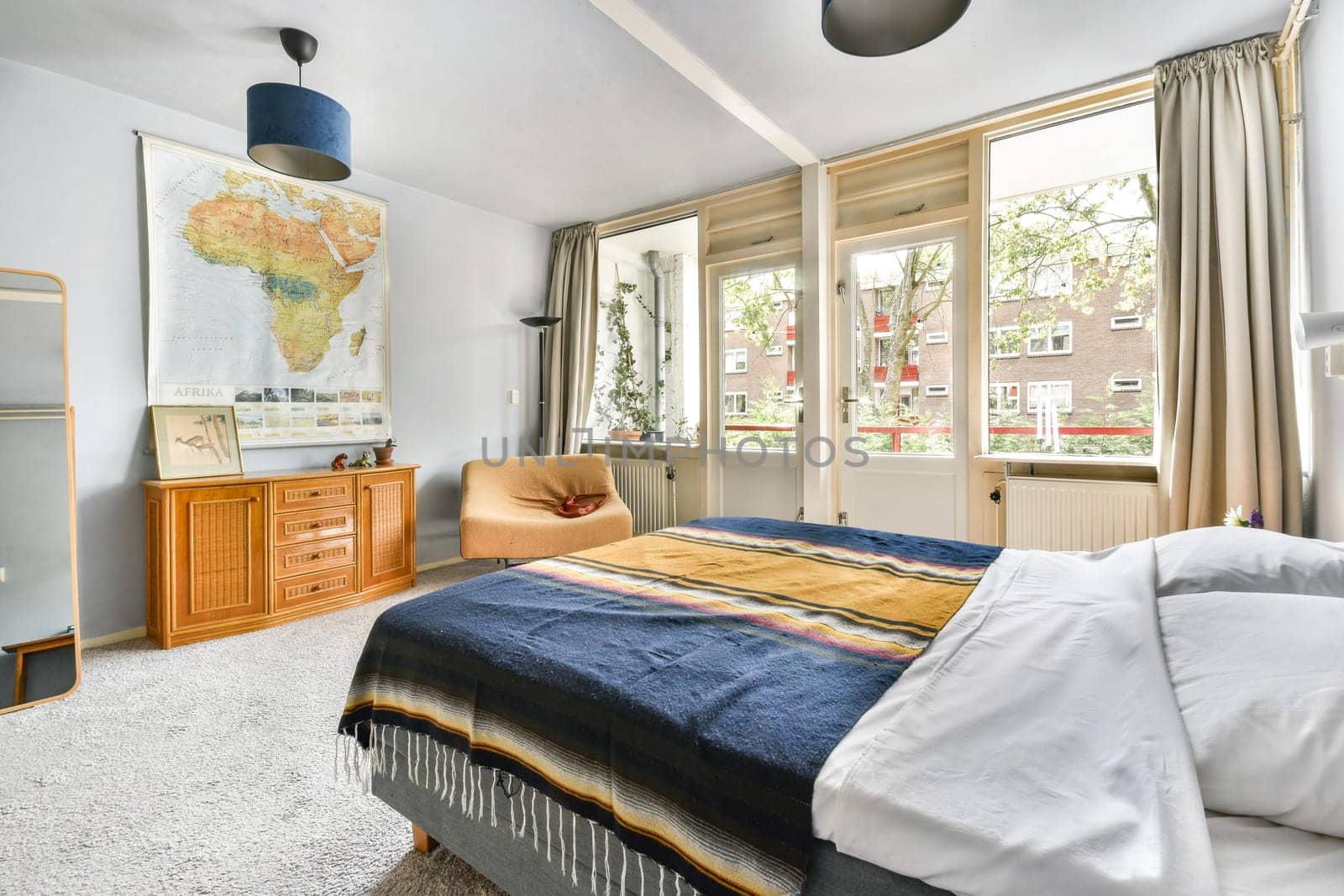 A serene bedroom interior featuring a world map, stylish furniture, and large windows allowing sunlight to fill the space beautifully.