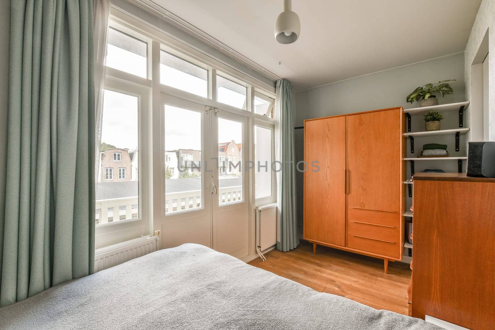 A serene bedroom featuring large windows that allow natural light to illuminate the space, complemented by wooden furniture and soft fabrics.