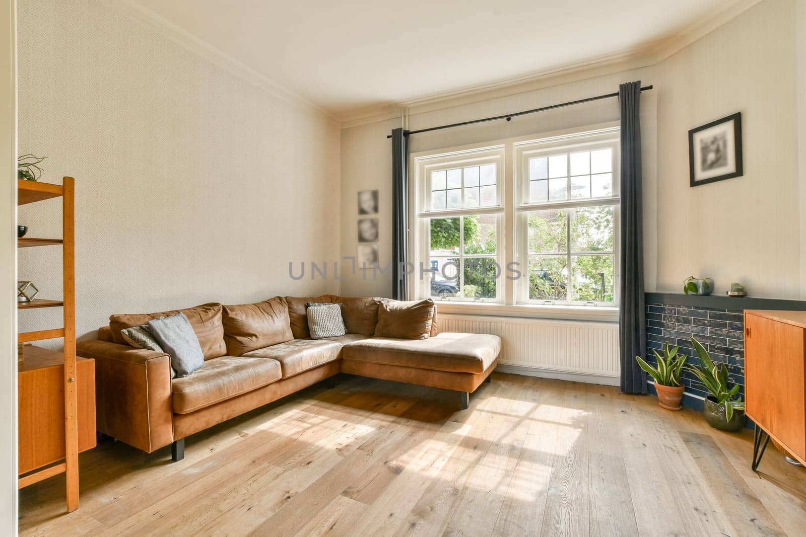 A contemporary living room featuring a brown leather sofa, large windows allowing natural light, and minimalistic decor to create a cozy atmosphere.