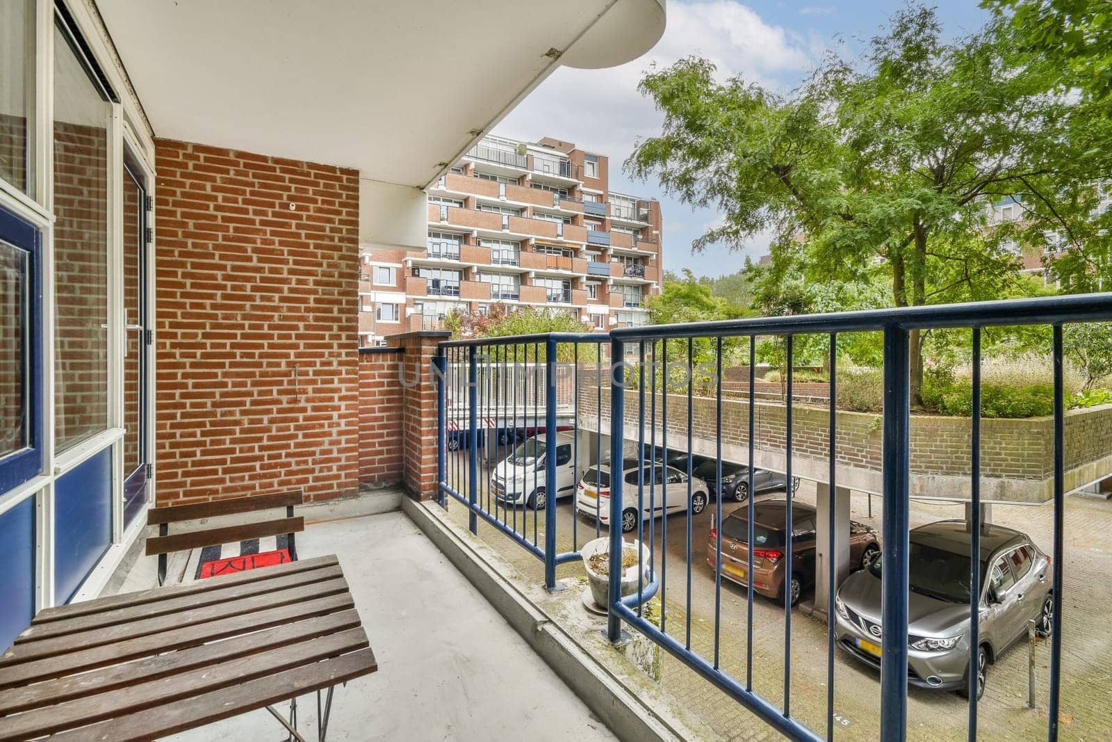 A scenic view from a modern apartment balcony, showcasing a vibrant landscape with trees and parked cars, creating a serene urban ambiance.