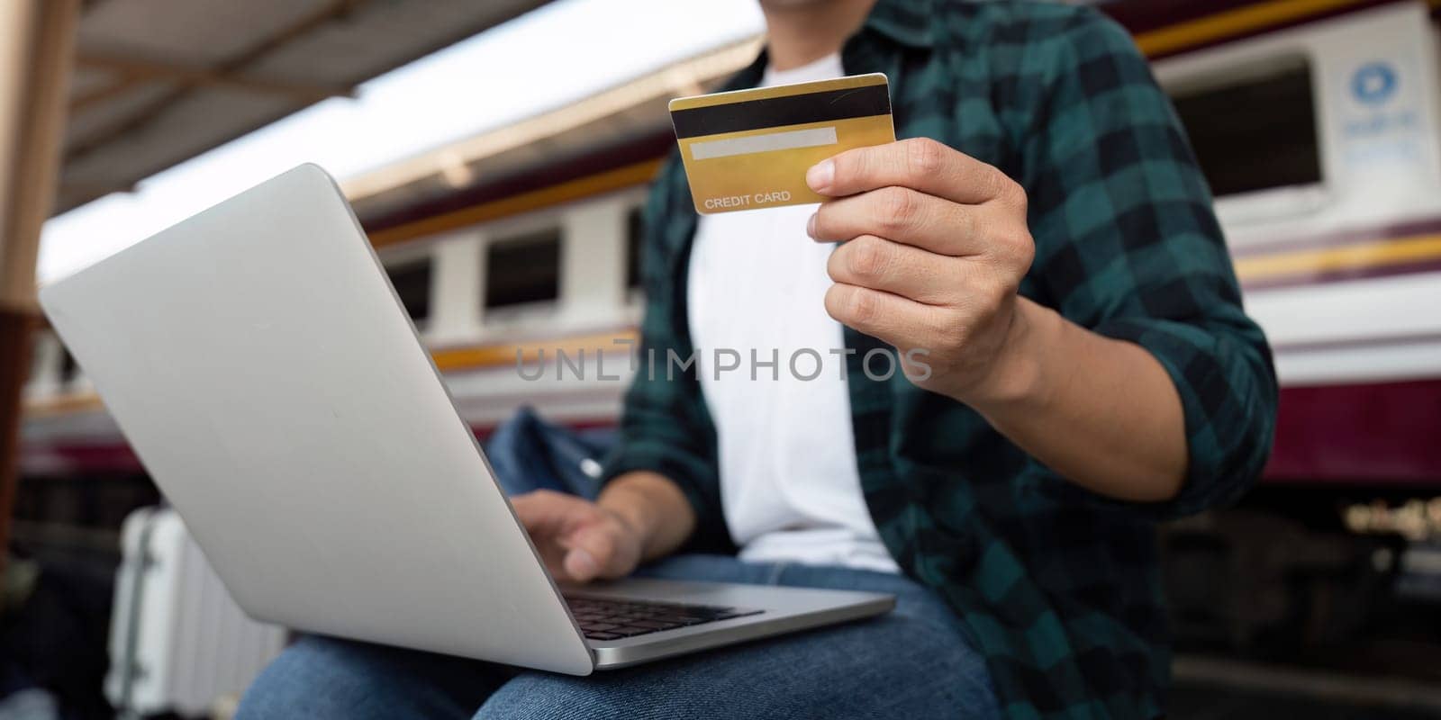 A young man prepares for bookings, showcasing his credit card while managing travel plans on his laptop, blending finance and travel.