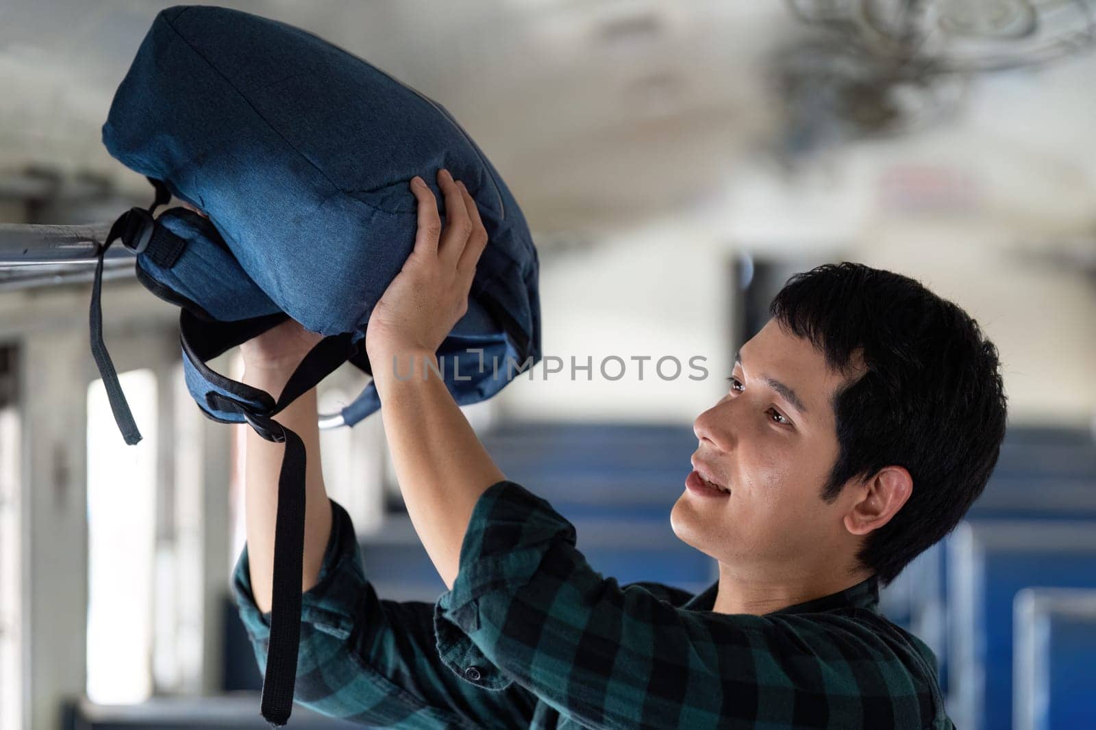 A focused traveler places his blue backpack into the overhead compartment of a bus, preparing for a journey filled with excitement.
