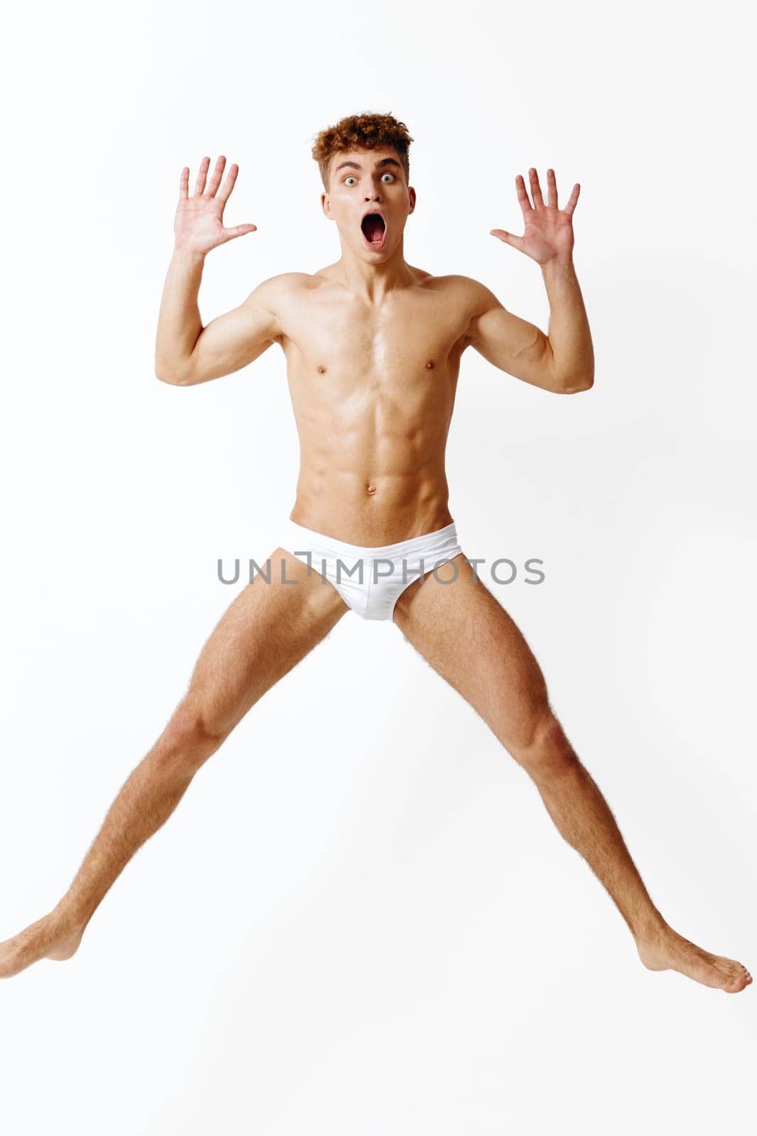 Dynamic young man with a surprised expression, leaping against a clean white background. A representation of freedom, joy, and spontaneity in a playful atmosphere.
