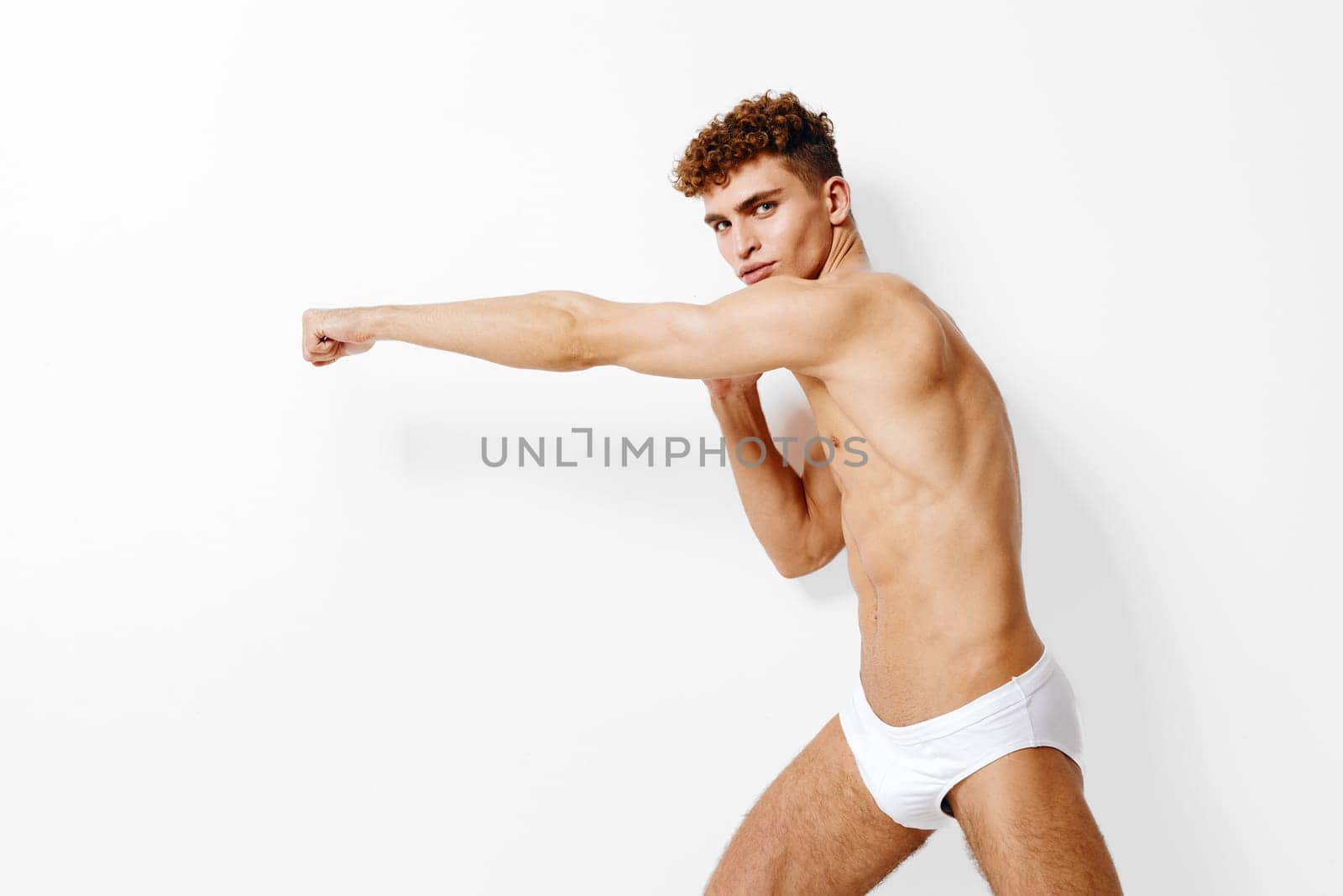 Focused young male model ready for a workout or boxing, showcasing strength and determination, set on a minimalist white background. Fitness and health lifestyle concept.