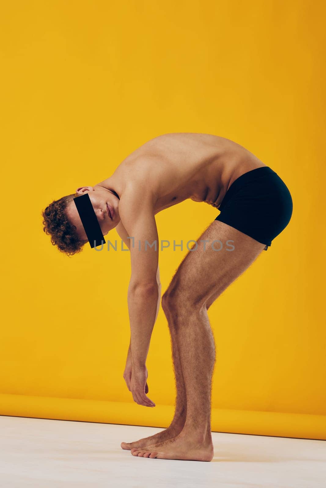 A fit male model demonstrating a unique pose, emphasizing physicality and form against a vibrant yellow backdrop, creating an engaging art concept.