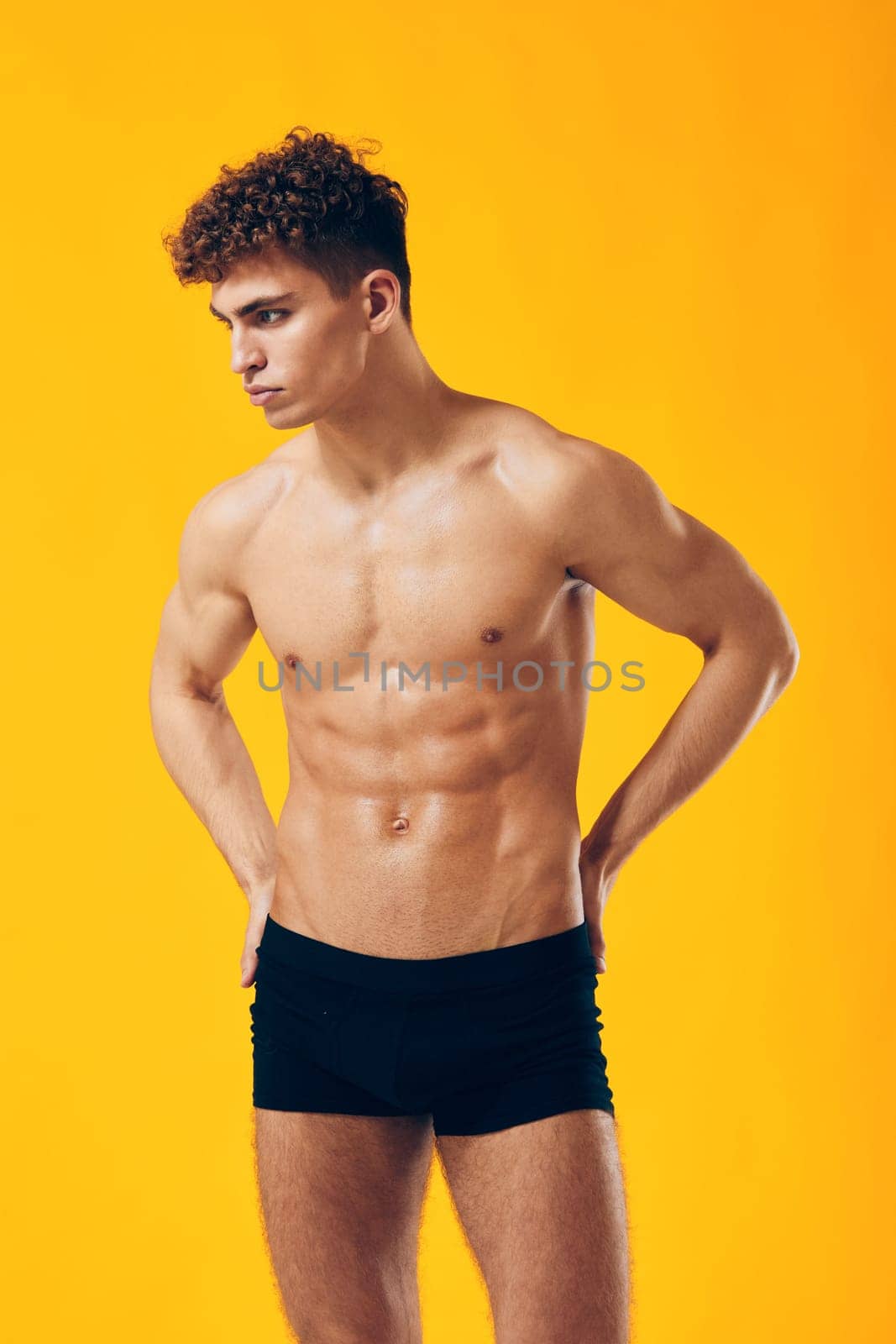 Posing male model demonstrating confidence and a healthy lifestyle with a toned body. Bright yellow backdrop emphasizes his physique, ideal for fitness and lifestyle concepts.