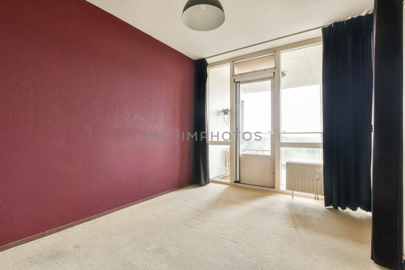 A serene interior showcasing a minimalist design with a burgundy accent wall, natural light streaming from the balcony, and soft textures on the floor.