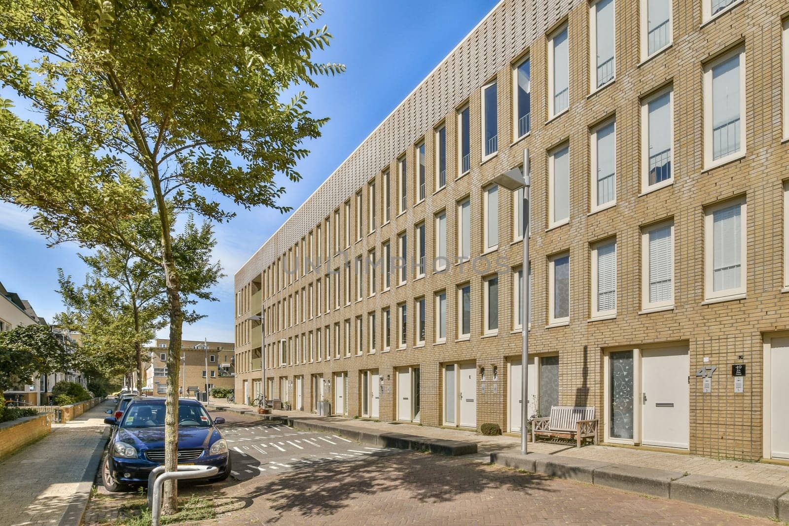 A striking modern building facade is framed by greenery and a pristine street. The architecture showcases large windows and a simplistic design.