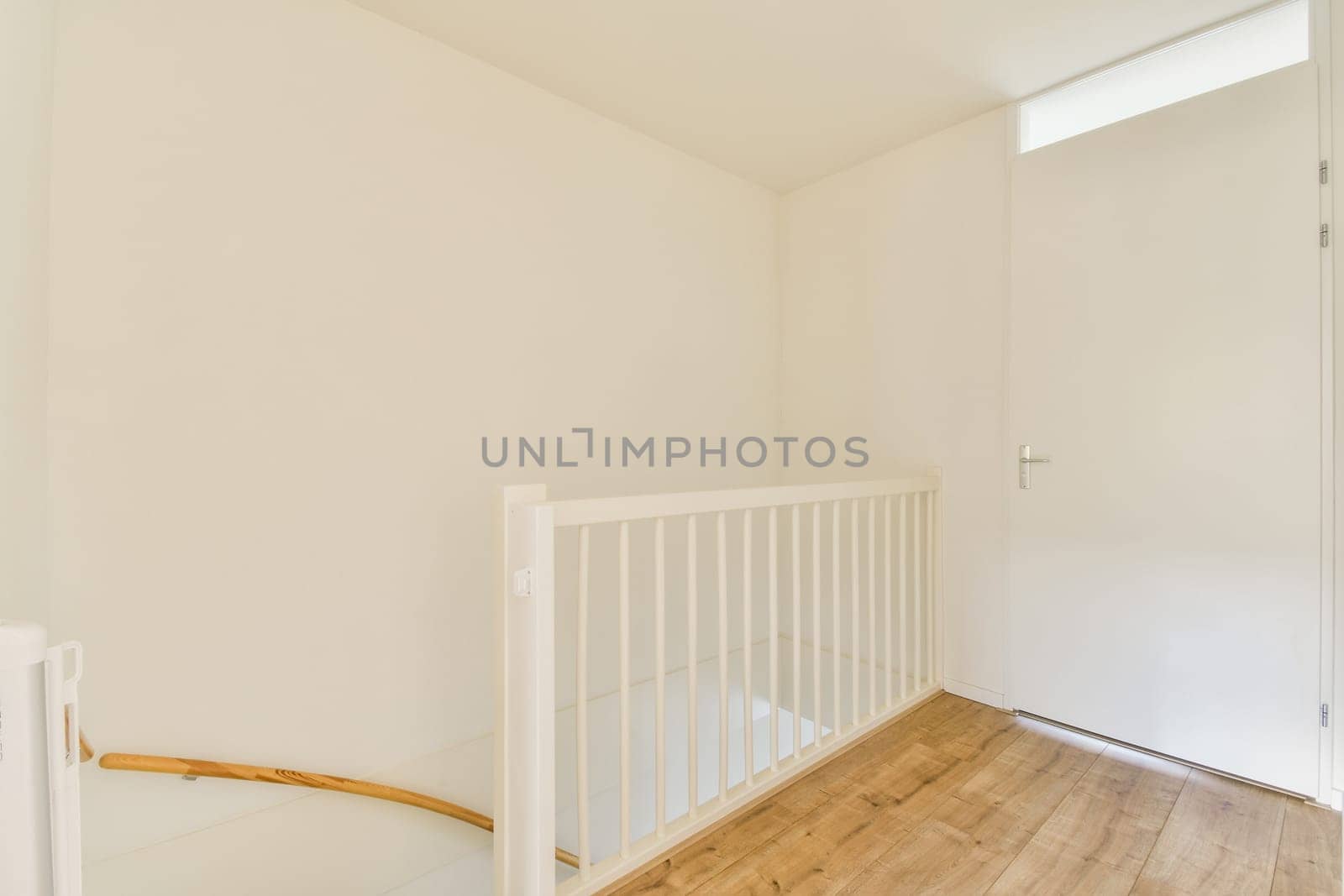 Bright and airy interior featuring a white color scheme with wooden flooring. The space includes a simple railing and a door, ideal for modern living.