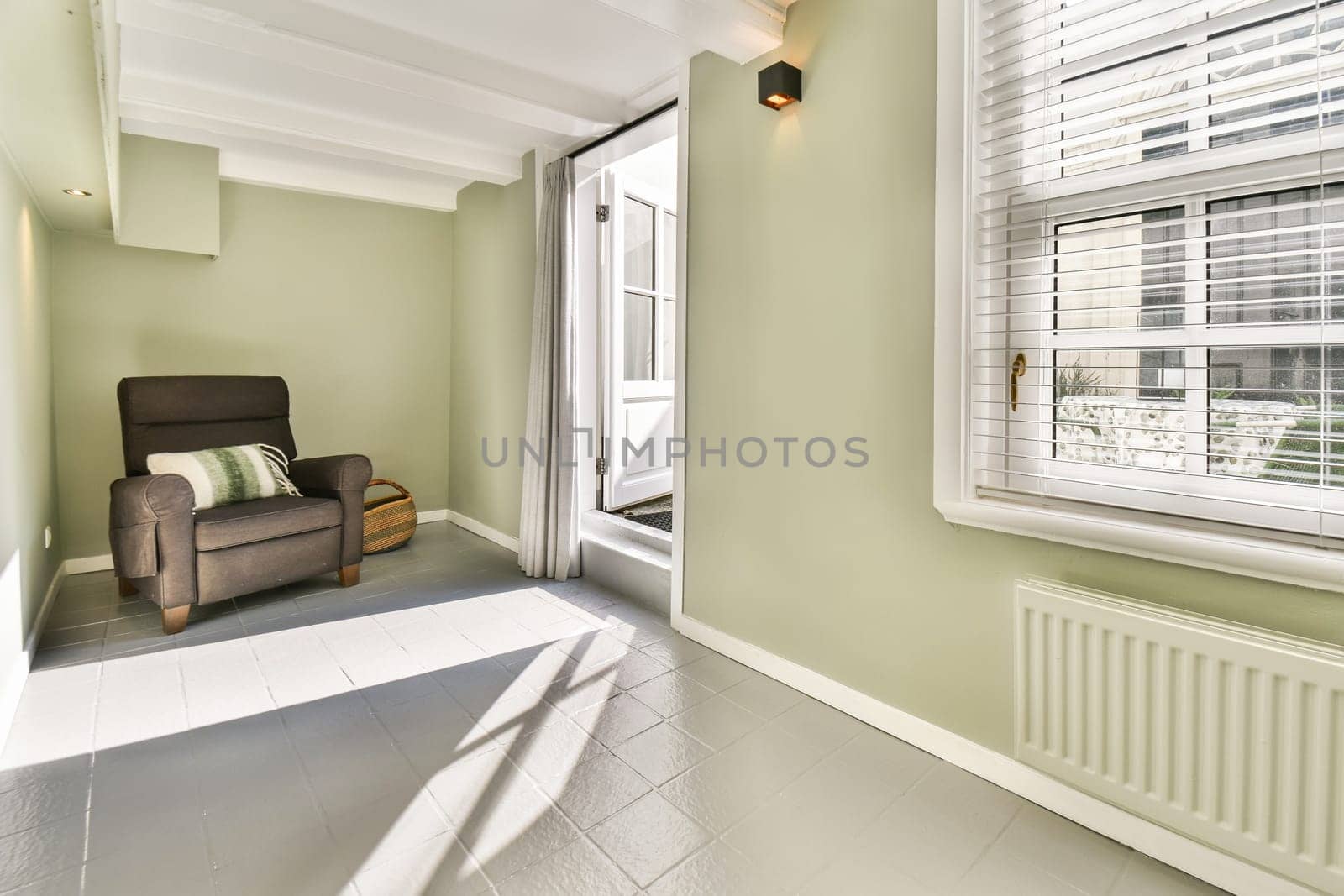 A bright and inviting interior featuring a comfortable chair, light green walls, and warm sunlight streaming through the window, creating a serene atmosphere.