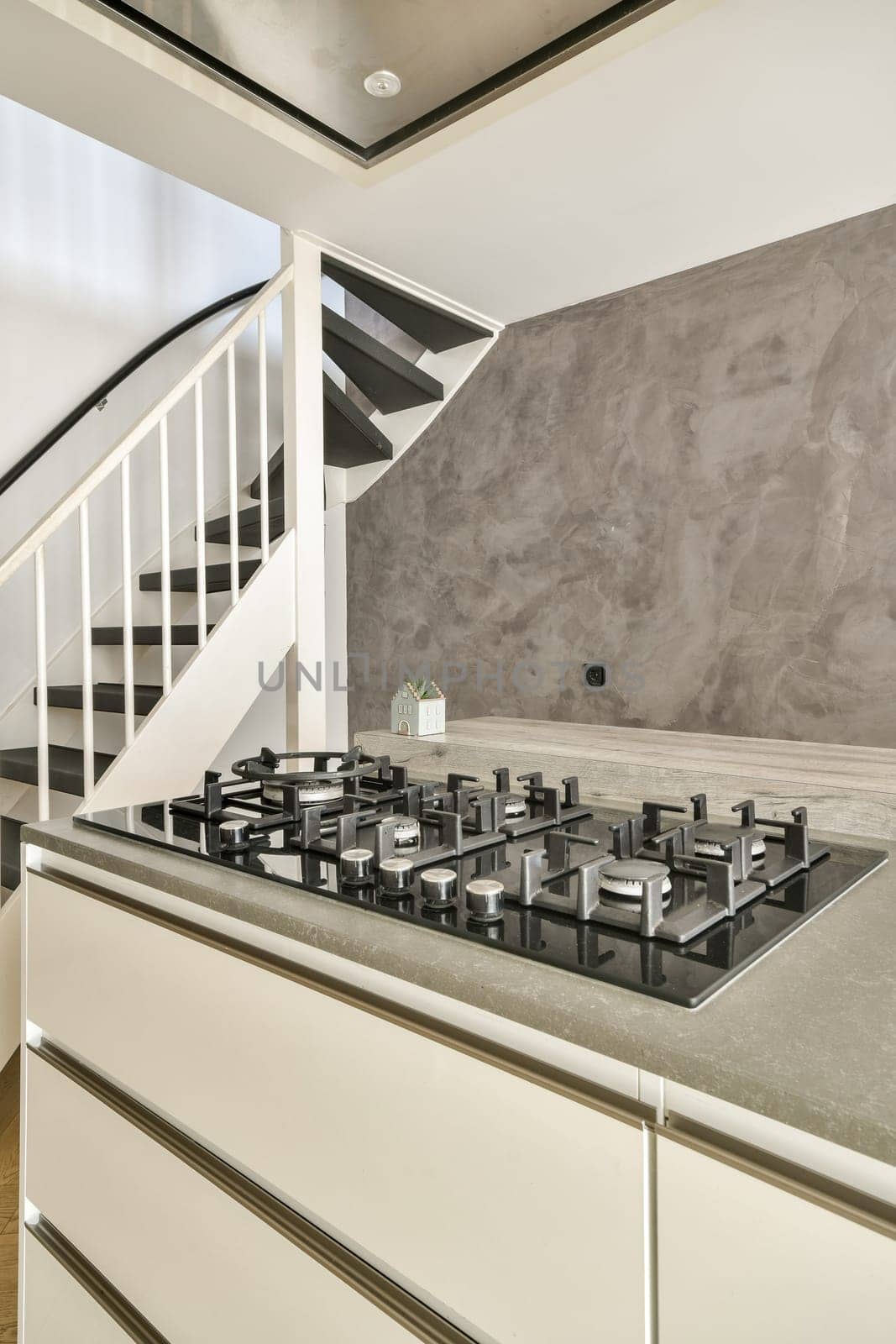 A contemporary kitchen featuring a sleek gas cooktop, elegant cabinetry, and a stylish staircase. The design highlights modern aesthetics and functionality.
