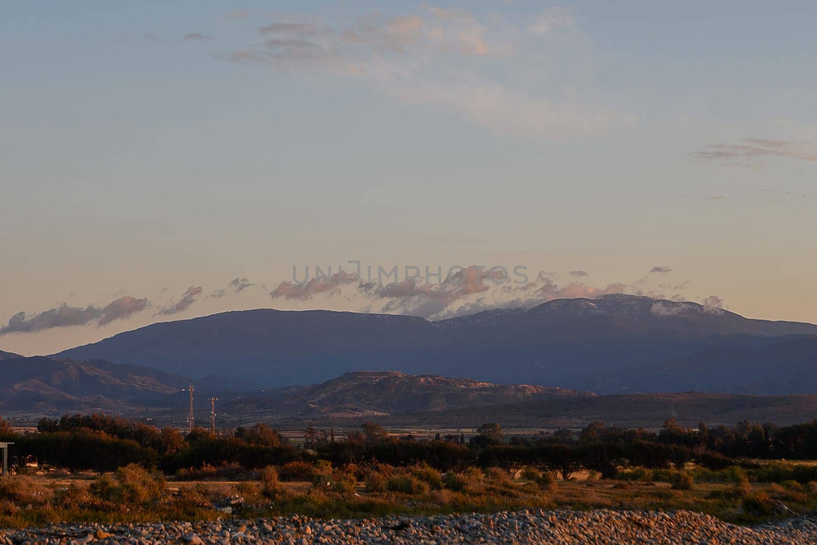 Golden hues from the sunset bathe the mountains in warm light, as soft clouds drift above the serene landscape. Nature's beauty unfolds in a tranquil evening setting that captivates the viewer.