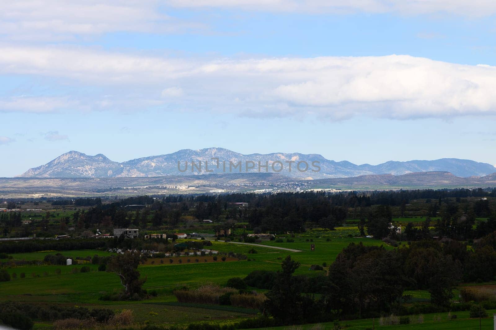 Expansive green valleys stretch beneath towering Andean peaks, where clouds drift lazily across a vibrant blue sky. Nature’s tranquility envelops the captivating scenery.