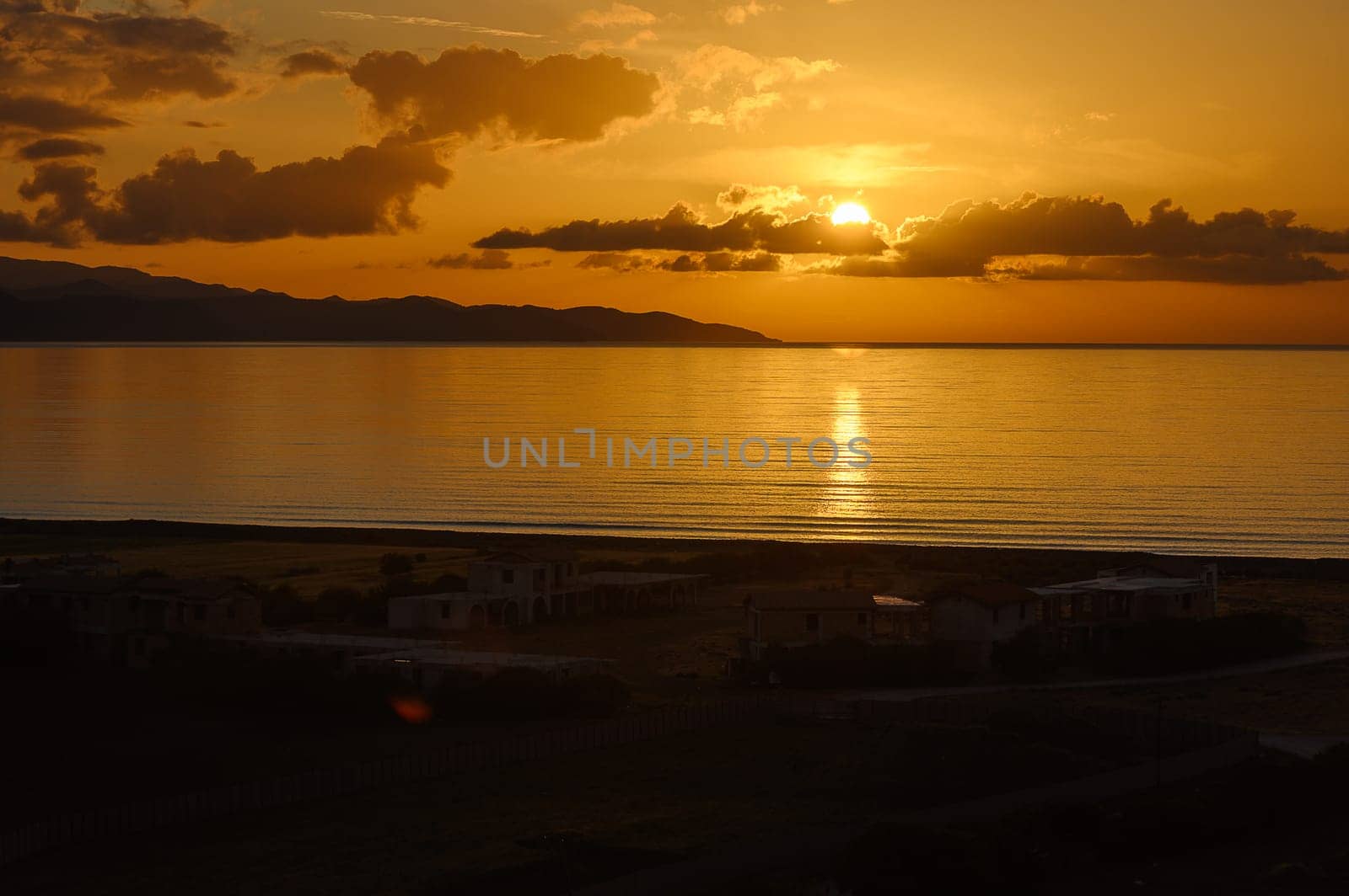 As the sun rests on the horizon, golden hues spread across the sky and water, illuminating the serene landscape. A peaceful moment captures the day's end in a coastal paradise.
