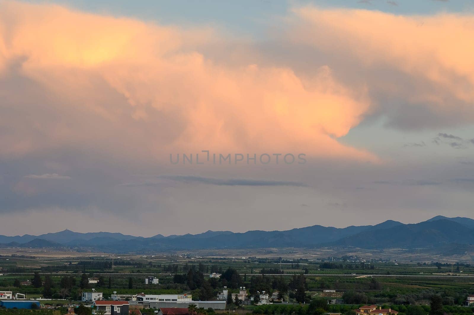 As dusk approaches, enchanting clouds fill the sky, painting it in pastel shades over the distant mountains. Below, lush fields extend towards a peaceful horizon, fostering a sense of calm.
