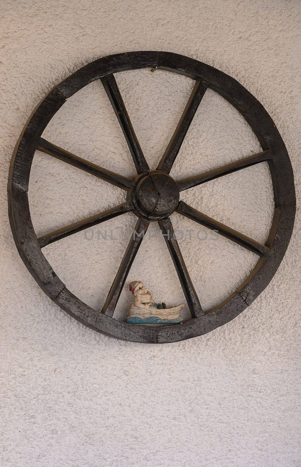 A rustic wooden wheel hangs on a textured wall, showcasing a charming shoe figurine positioned at its center. This unique blend of craftsmanship and art draws the eye with its intriguing details.