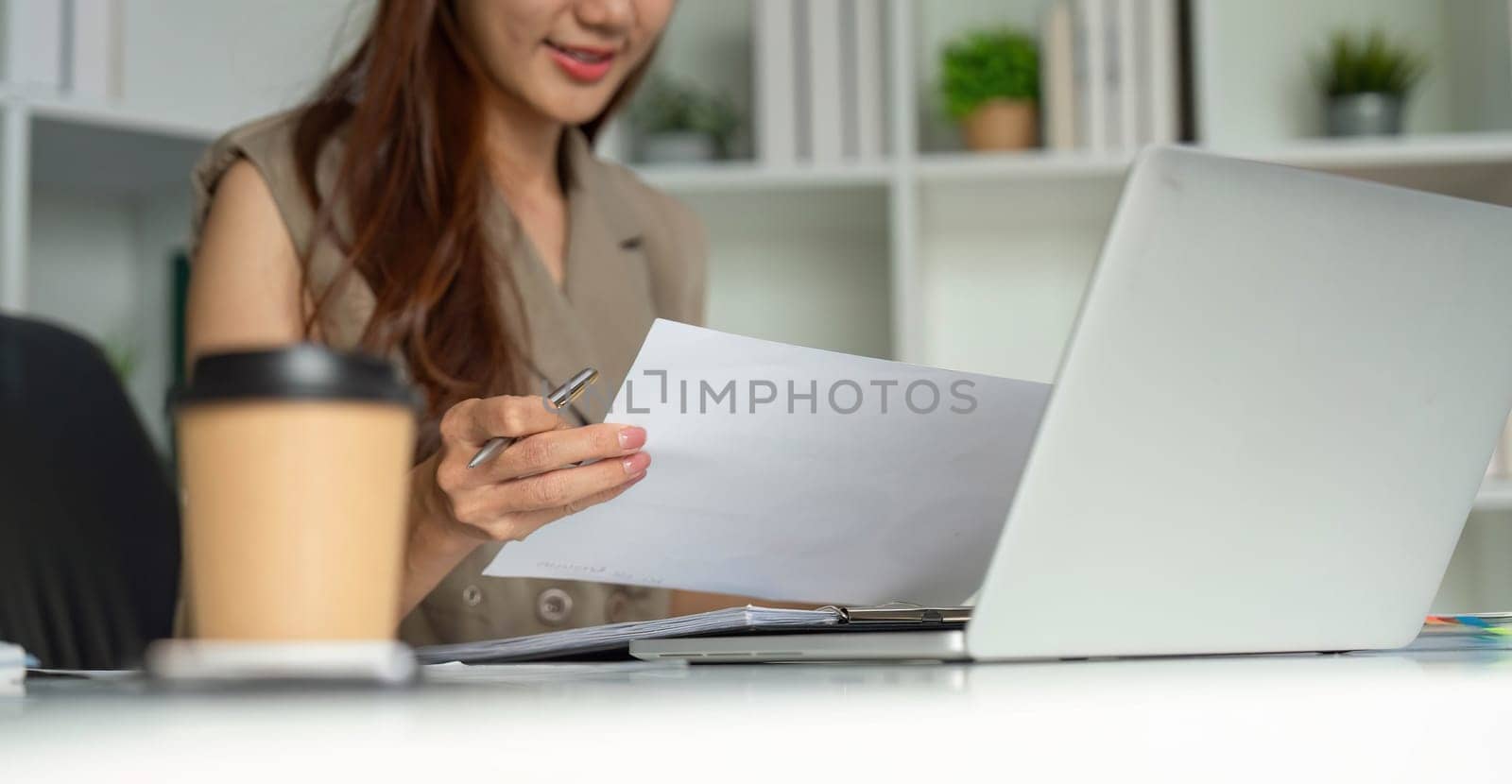 The woman holds papers in hand while reviewing her notes, exemplifying a proactive approach to her business tasks in a well-organized office environment.
