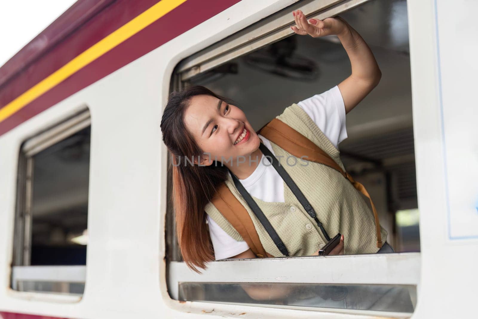 With a playful expression, she enjoys the wind in her hair as she peeks out from the train window, embracing the travel adventure.