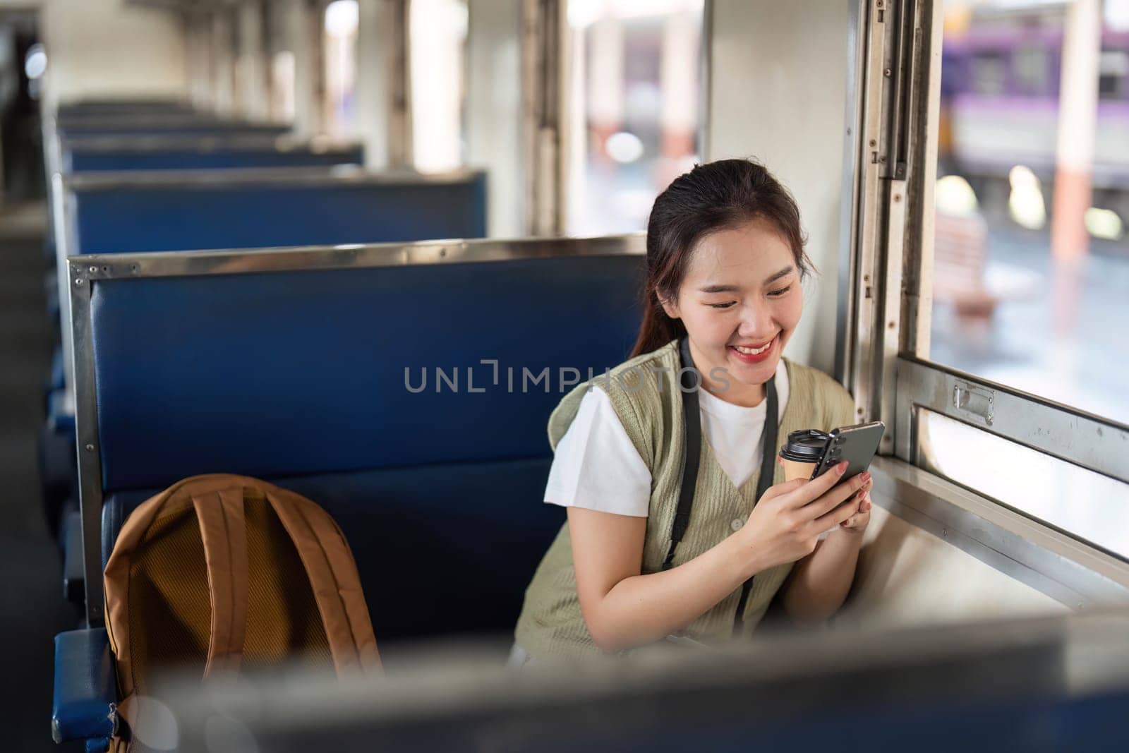 A cheerful traveler engaged with her smartphone as she relaxes in her train seat, combining modern communication with the joys of travel.