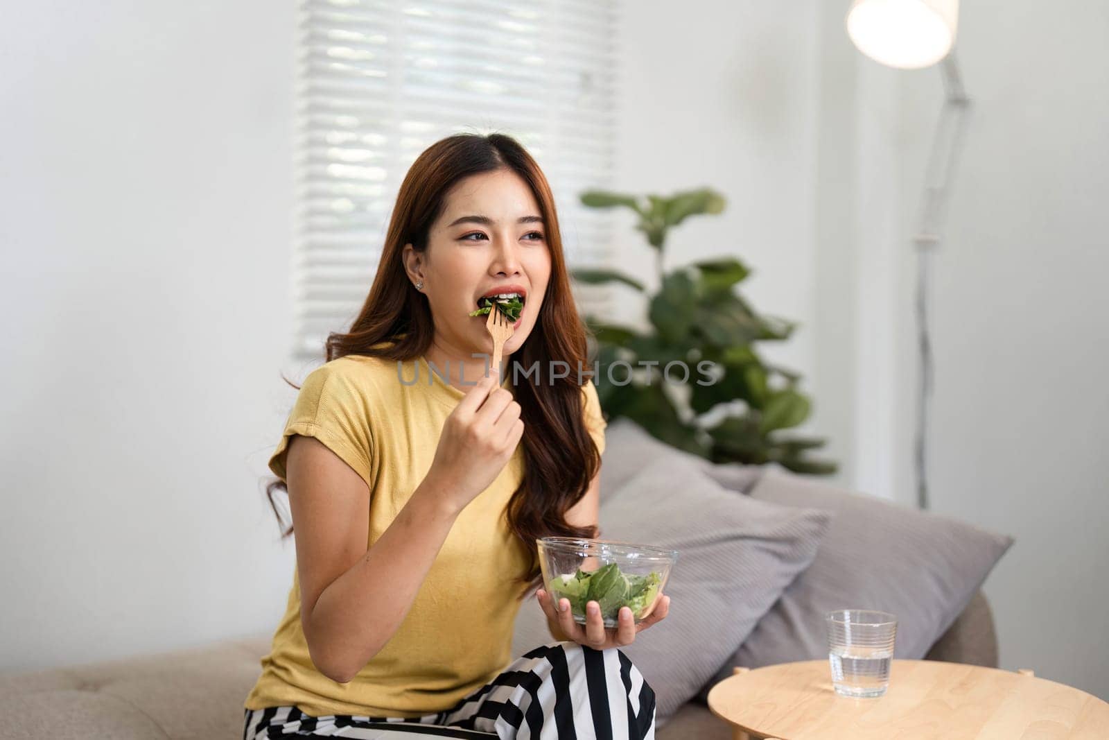 In a serene setting, a woman takes a moment to enjoy her salad, making the most of her morning downtime for self-care and nourishment.