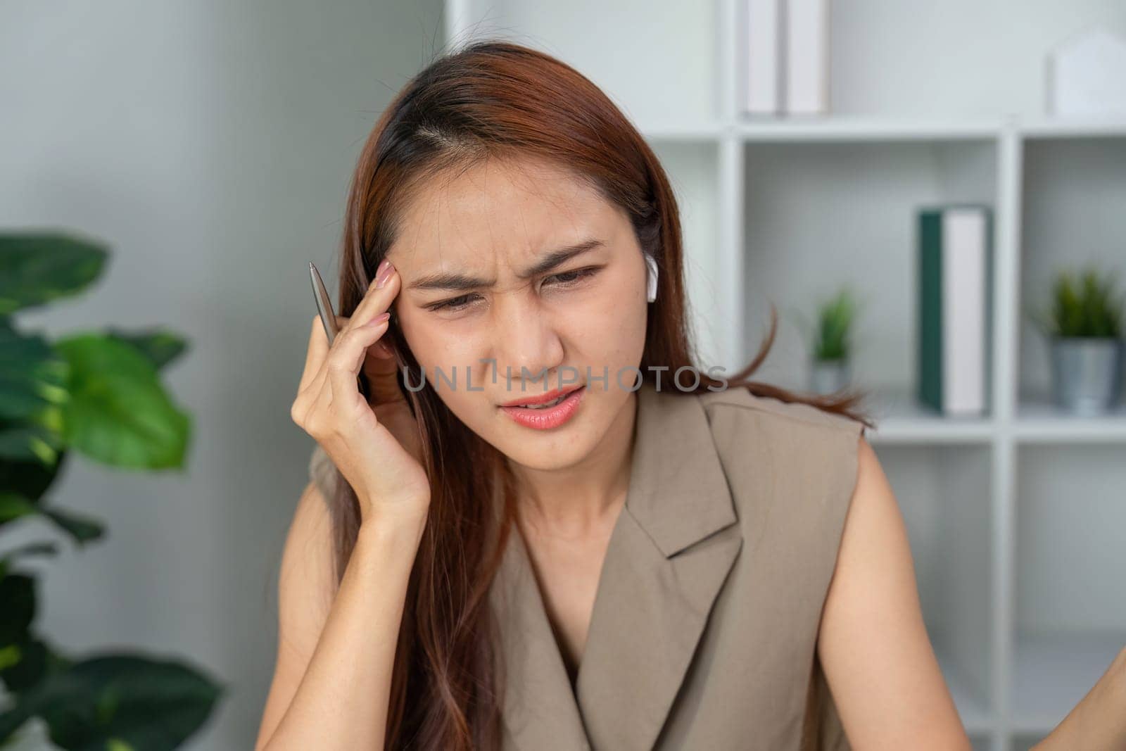 The woman touches her head in contemplation while managing tasks, signifying the importance of mental health in a professional setting.