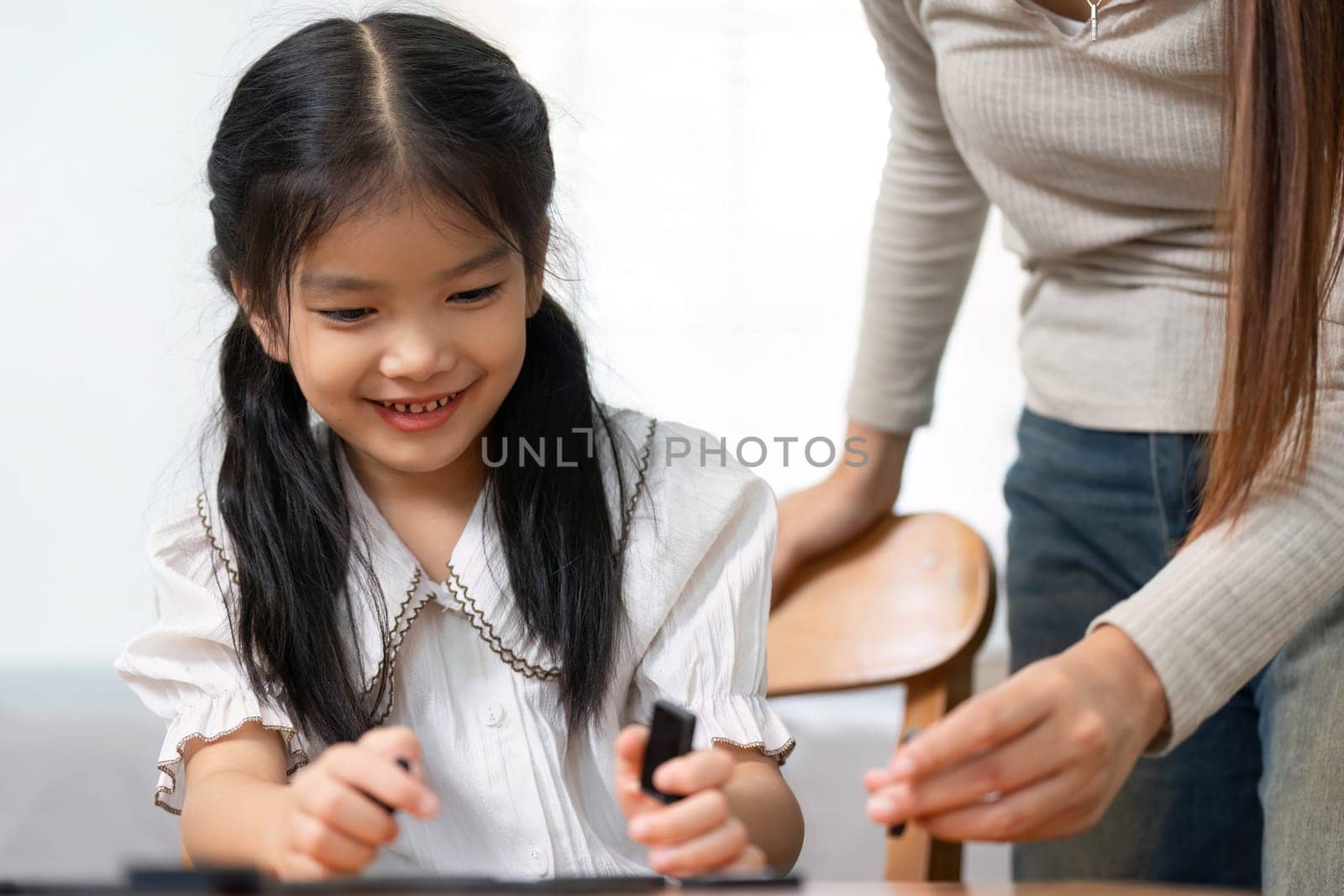 A young girl smiles brightly as she plays a game with her mother, highlighting the importance of family time and simple joys in childhood.