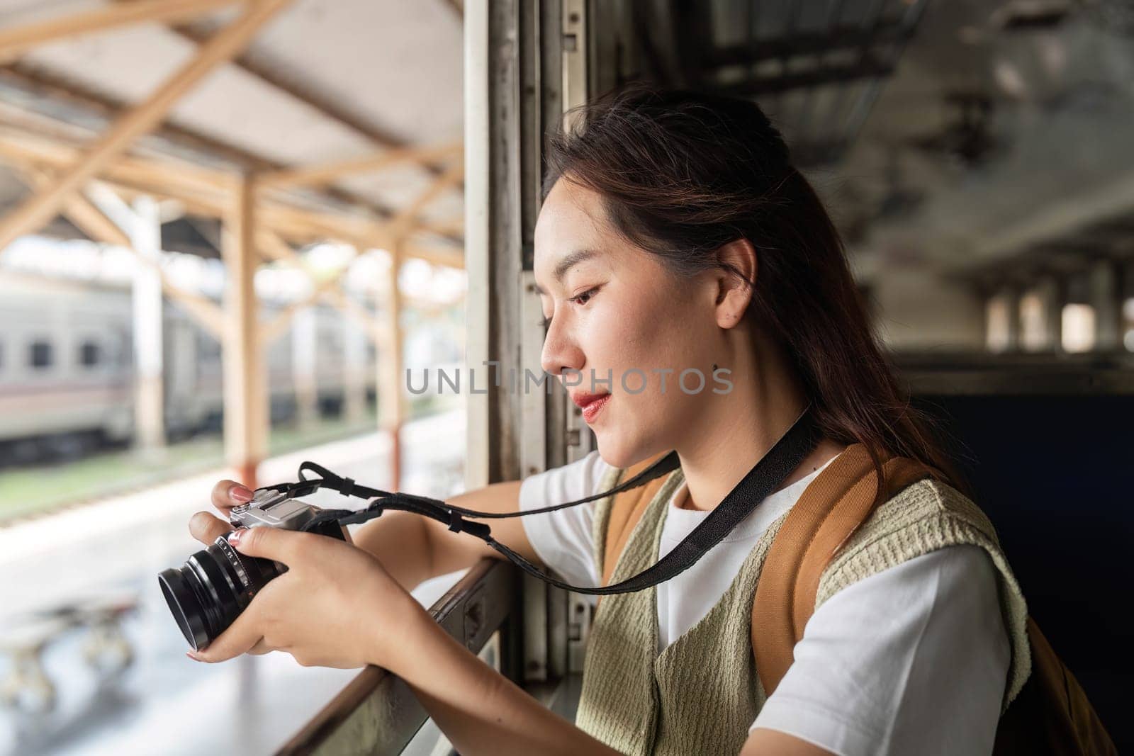 A traveler sits by the train window, focused on her camera, eager to capture the beauty outside during her journey.