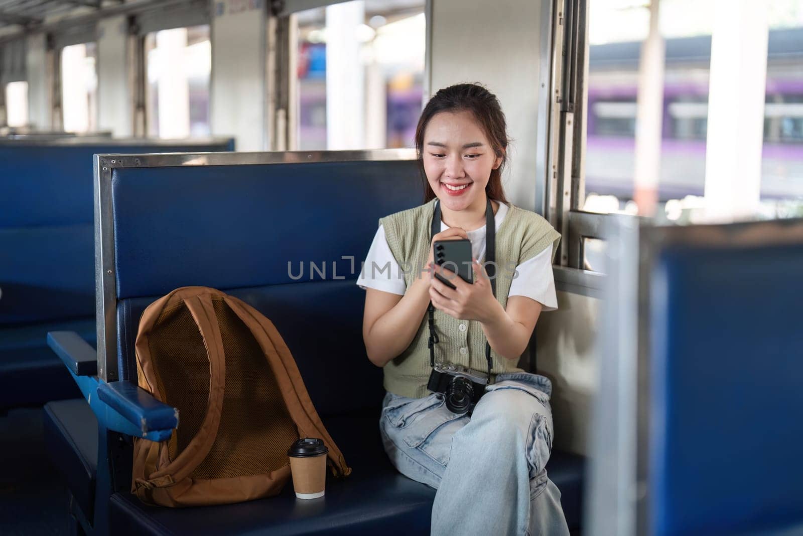Relaxing on a train, a young woman is engaged with her smartphone, smiling while enjoying her travel experience.