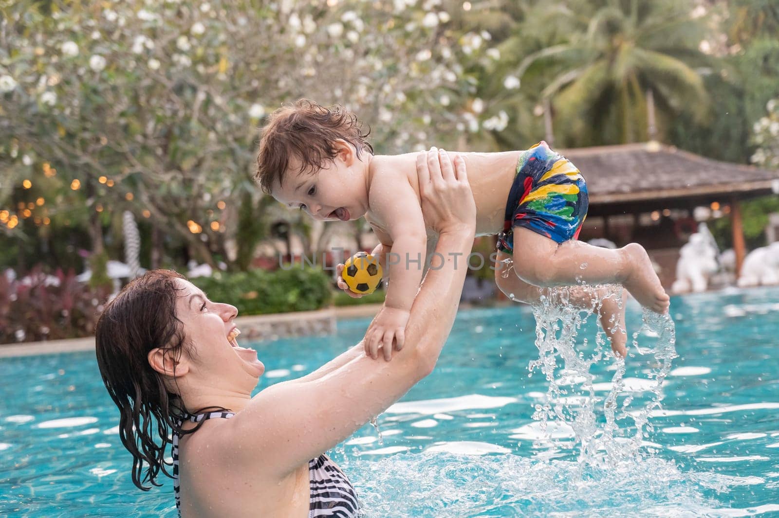 Caucasian woman holds son while swimming in pool on vacation