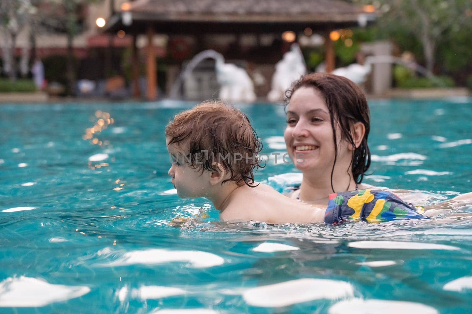 Caucasian woman holds son while swimming in pool on vacation