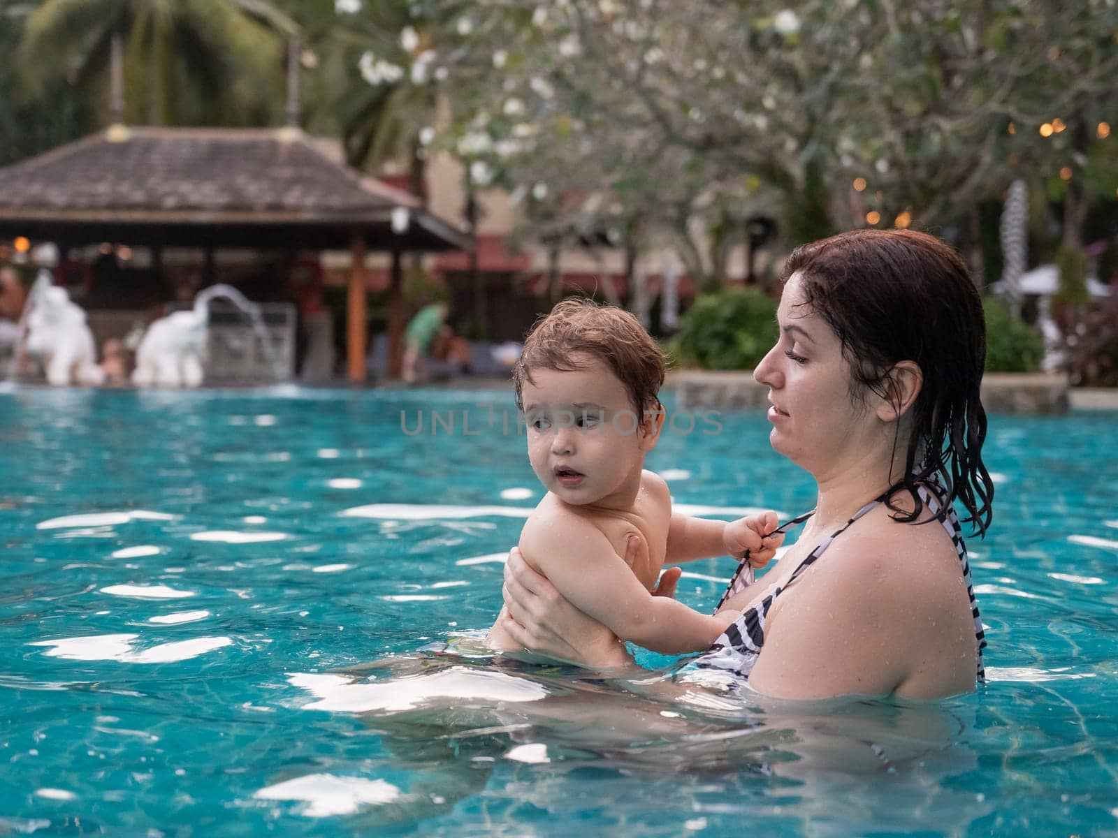 Caucasian woman holds son while swimming in pool on vacation