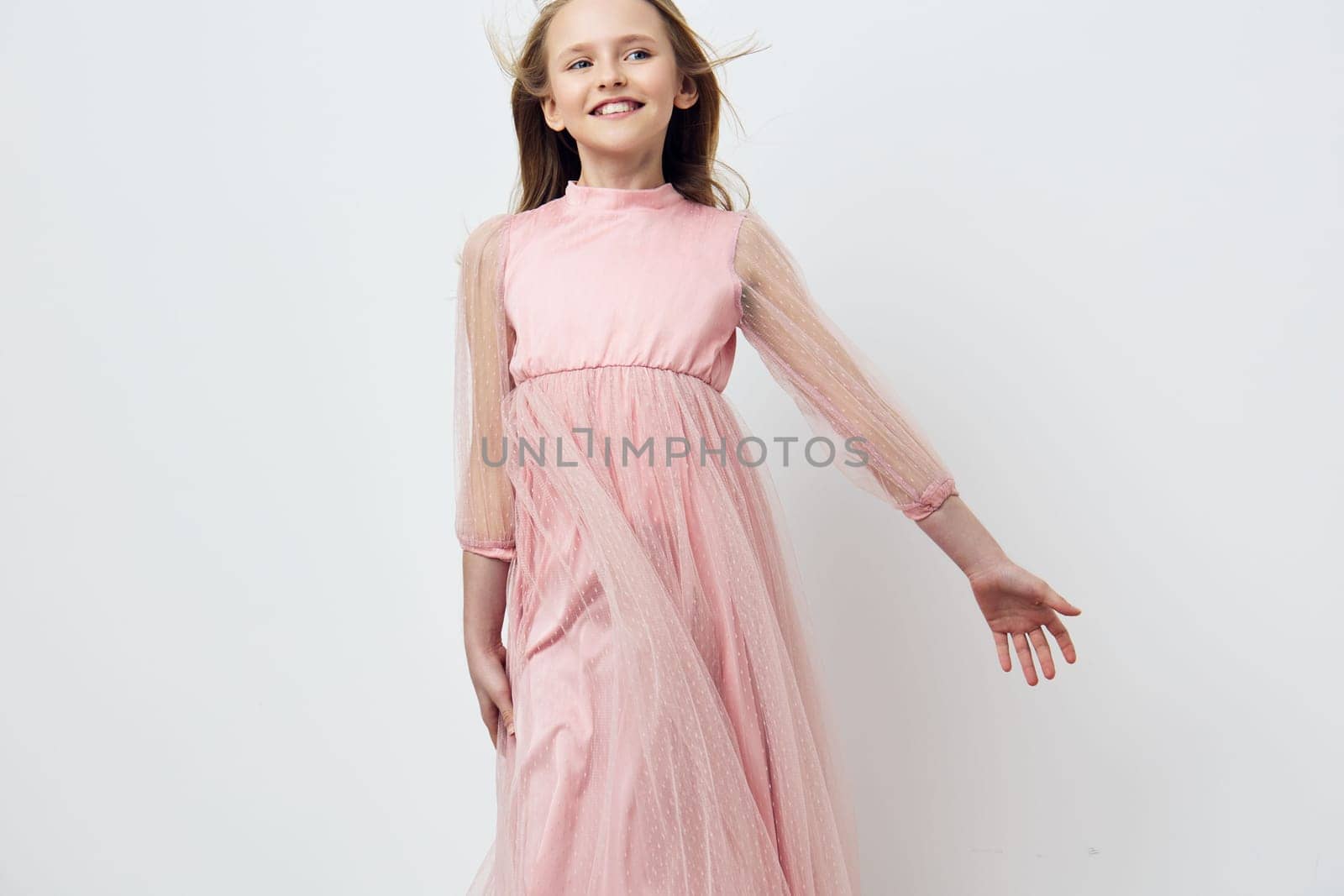 A cheerful young girl dressed in a flowing pink gown with sheer sleeves, exuding happiness in a pastel colored scene, perfect for children s fashion or joyful celebrations