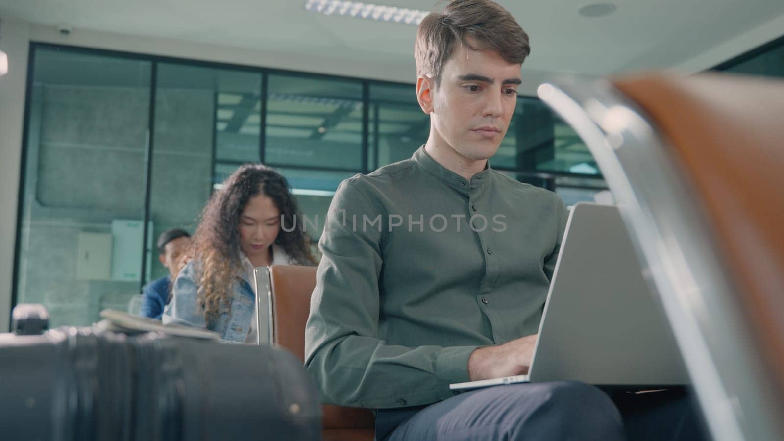 Young handsome man with a suitcase sitting working his laptop at airport terminal hall while waiting landing for her flight, tourist men in international airport, travel trip