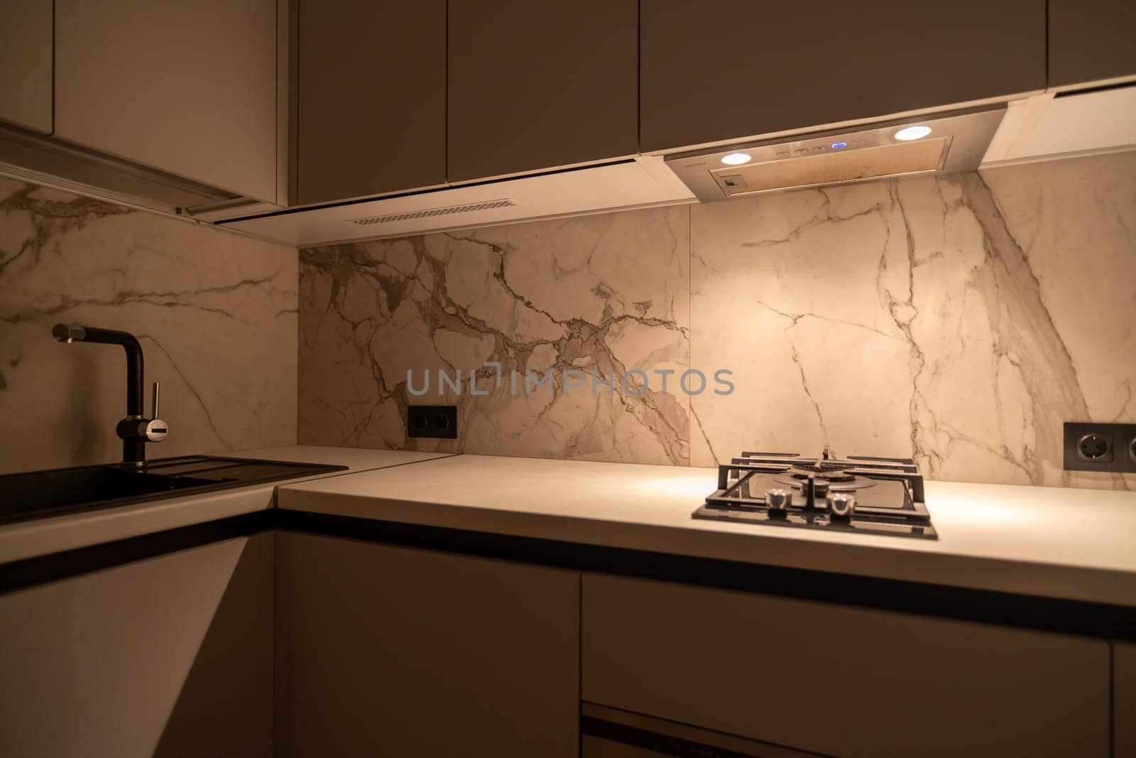 Modern kitchen backsplash featuring a large marble slab illuminated by recessed lighting. A gas cooktop and sleek sink are integrated into the minimalist countertop design.