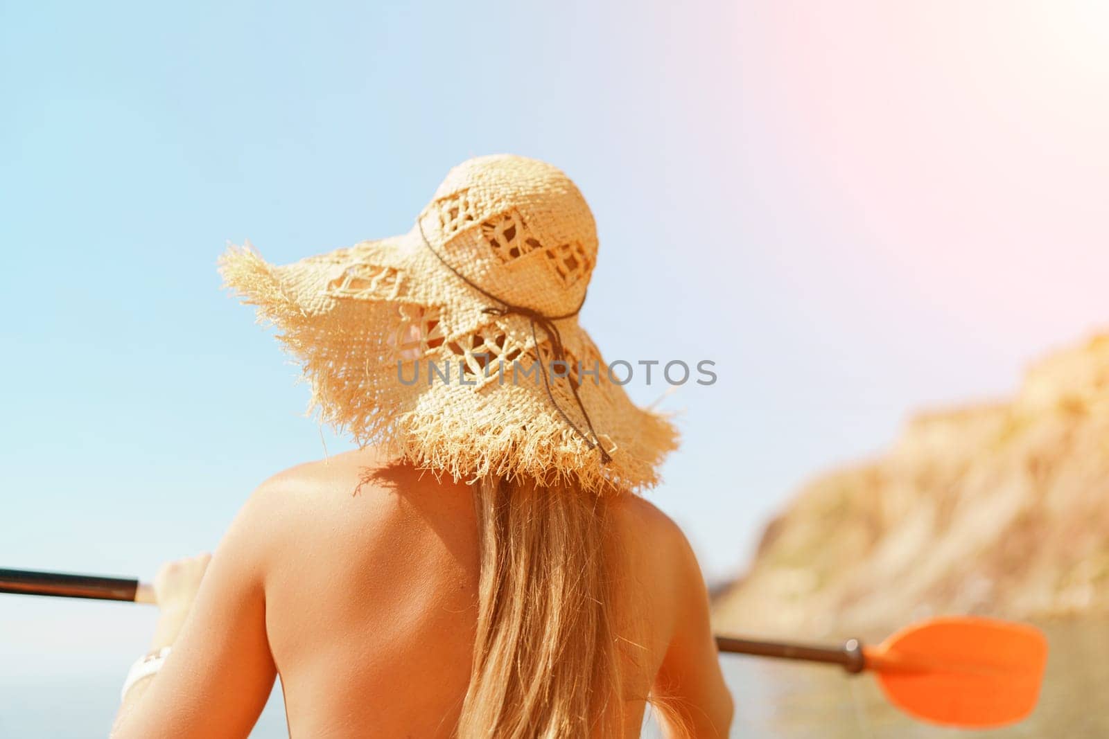 Woman in kayak back view. Happy woman with long hair in a swimsuit and hat floating in kayak on the sea. Summer holiday vacation. Summer holidays vacation at sea