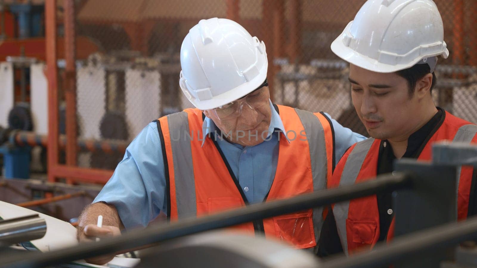 Engineer teaching apprentice to use metal sheet stamping machine, industrial team is working on various projects with tablet computer, worker work together to check the operation system in a factory