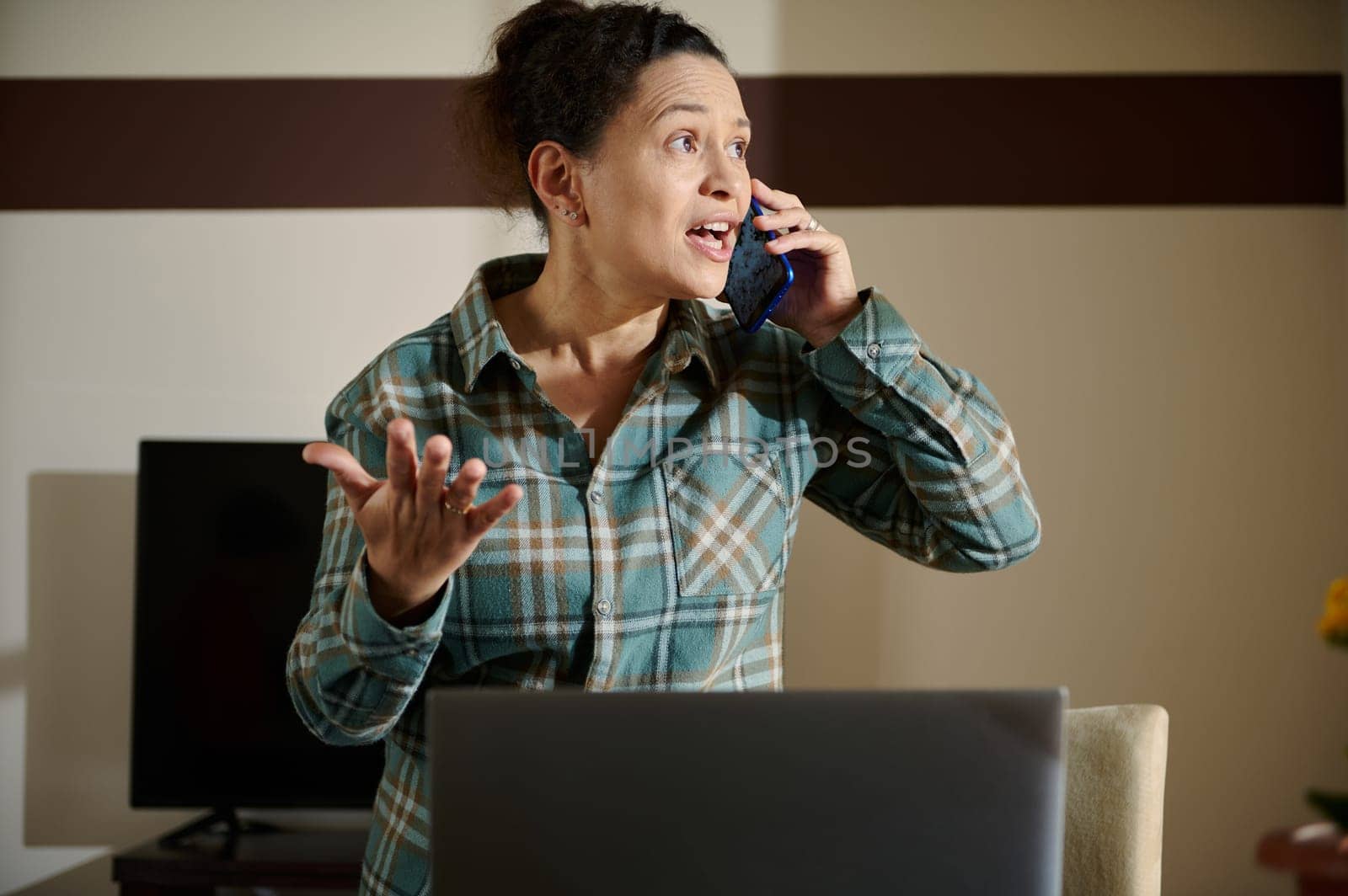 A woman in a home office setting having an engaging conversation on the phone, conveying determination and focus. The room features a laptop and thoughtful interior design, suggesting remote work.