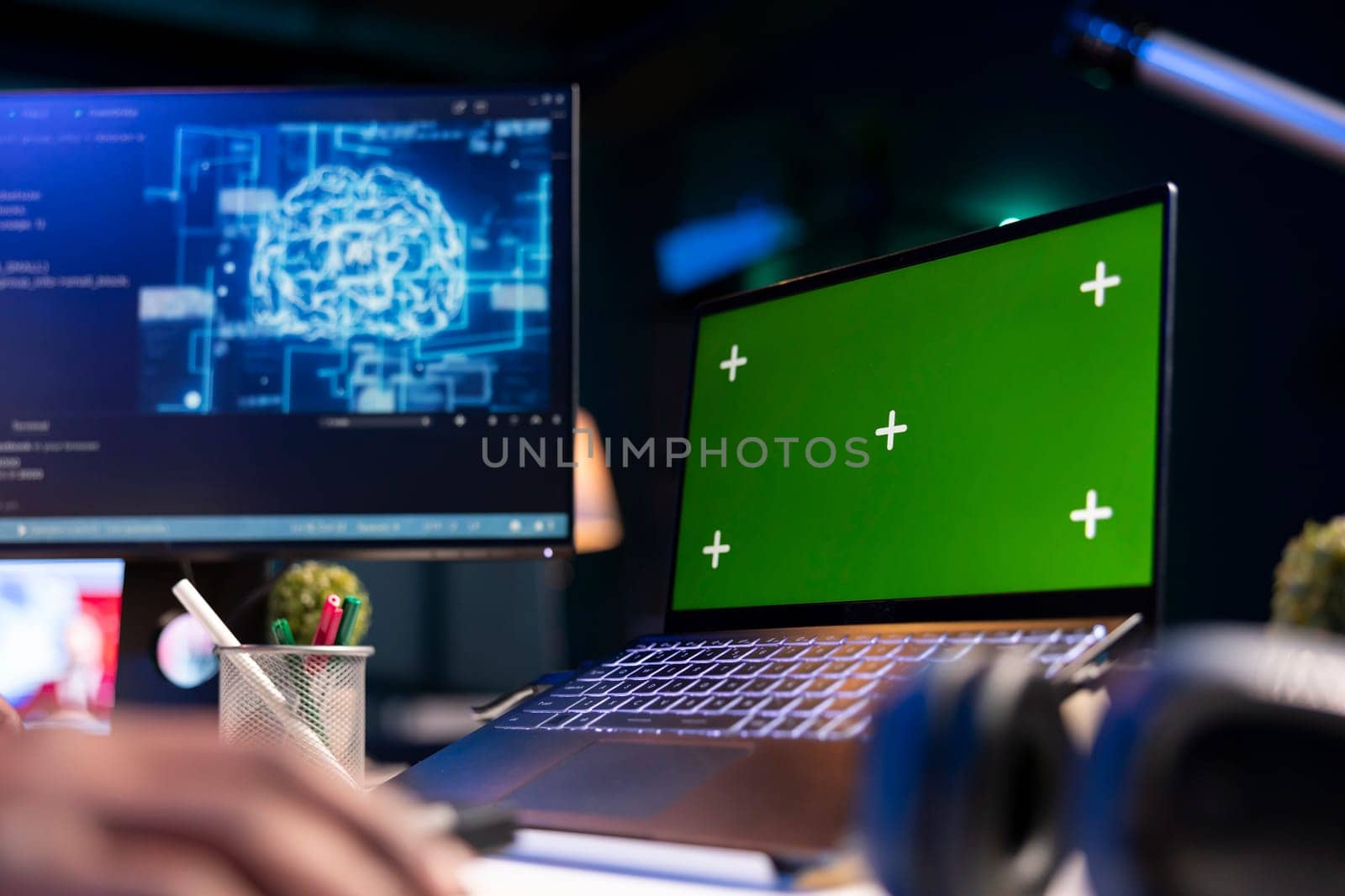 Black person programming neural network code with a green screen on computer to build databases. System engineer working from home while looking at data center security servers.