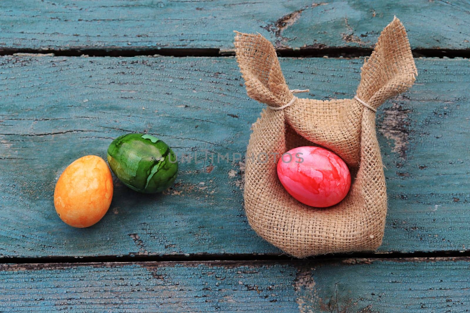 An Easter nest made from a jute sack with ears and colorful Easter eggs on a wooden base